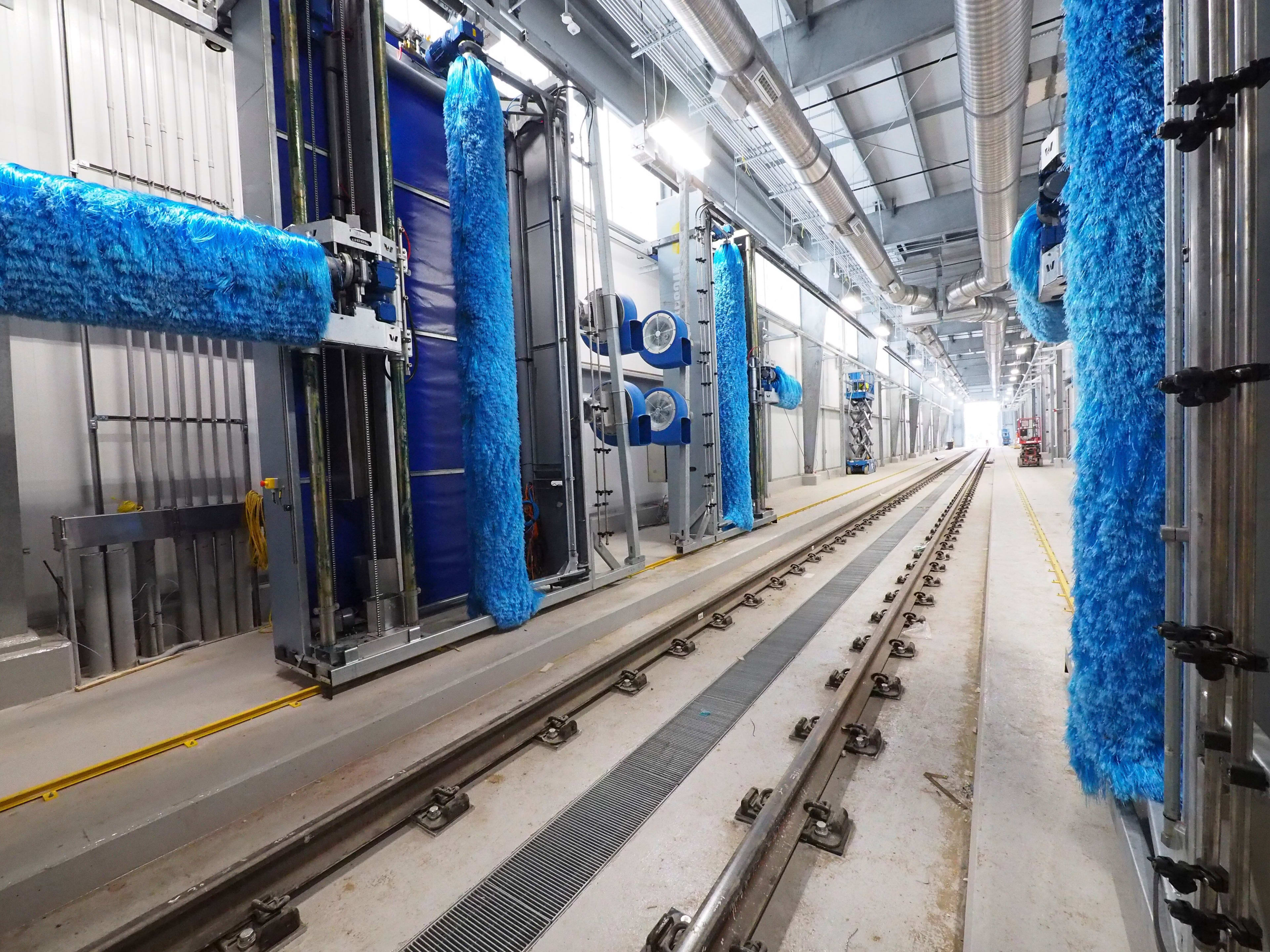 In what looks like a car wash for trains, large blue brushes sit on both sides of tracks in an in...