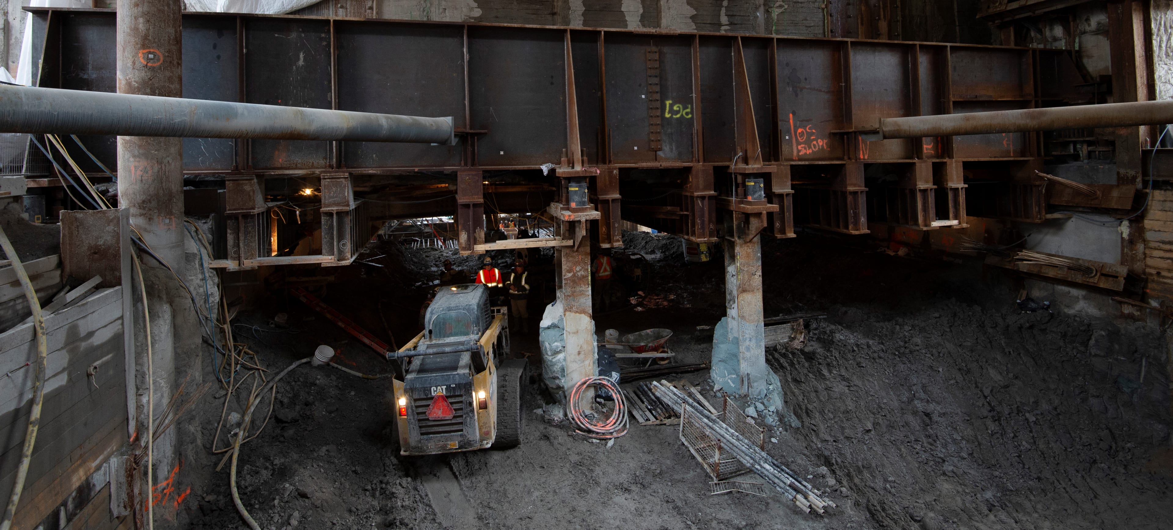 A tractor moves under a large girder.