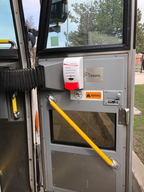 Image is a hand sanitizer machine attached to a bus door.