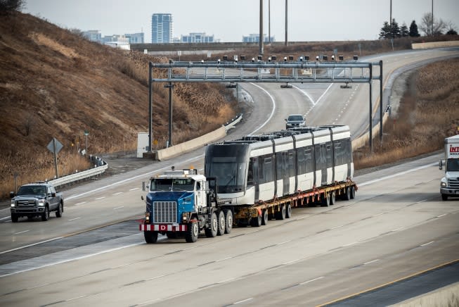 A photo shows an LRV on the back of a large flatbed truck, while driving on the highway.