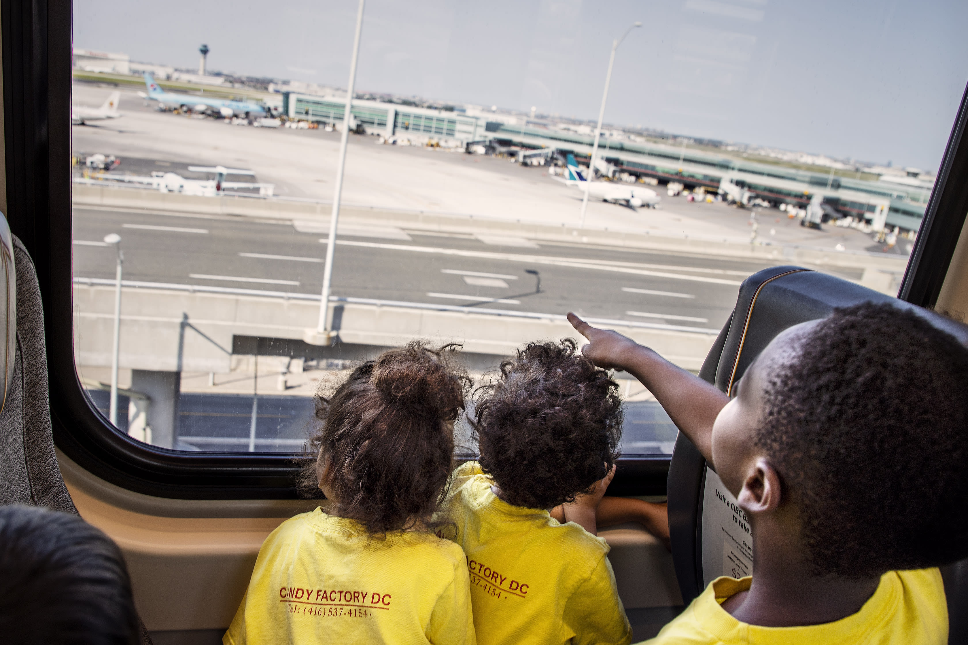 Children stare out the window toward the airport, and planes moving about.