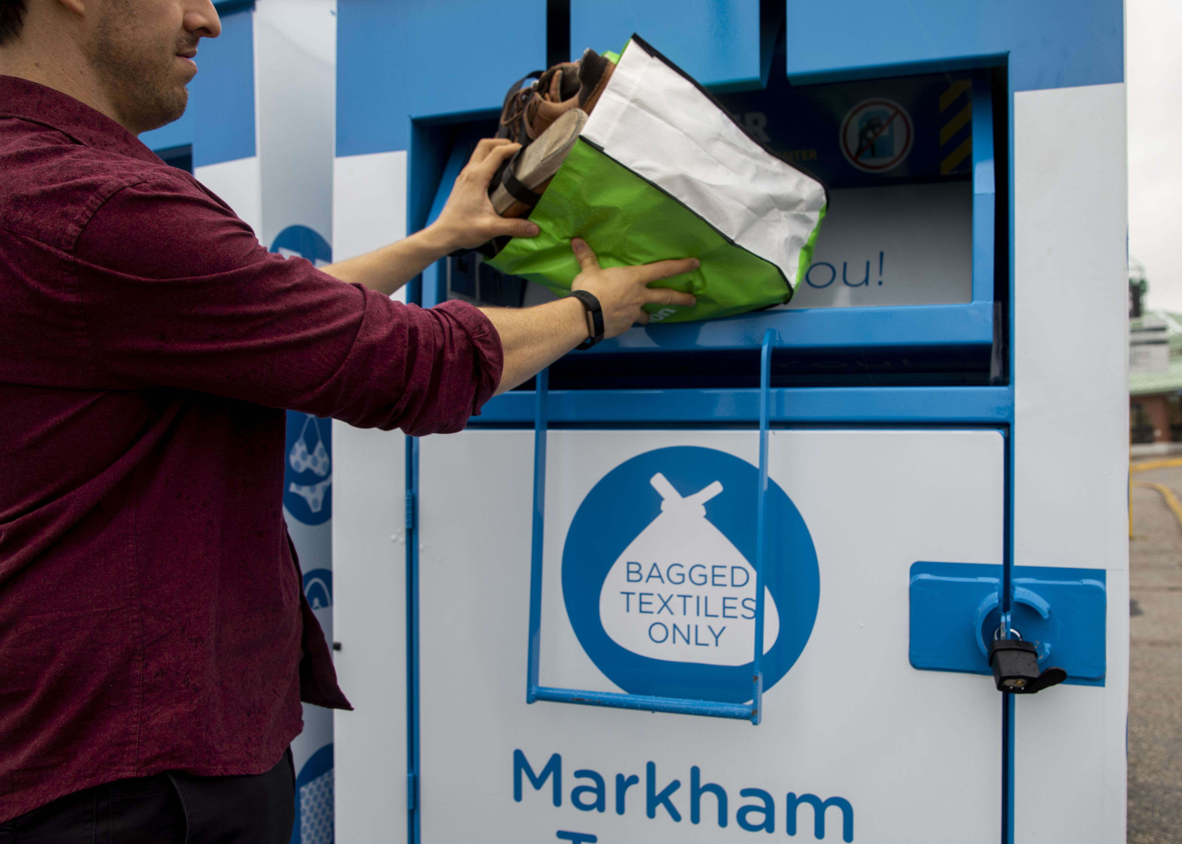 a person throwing a bag of clothes in a donation bin.