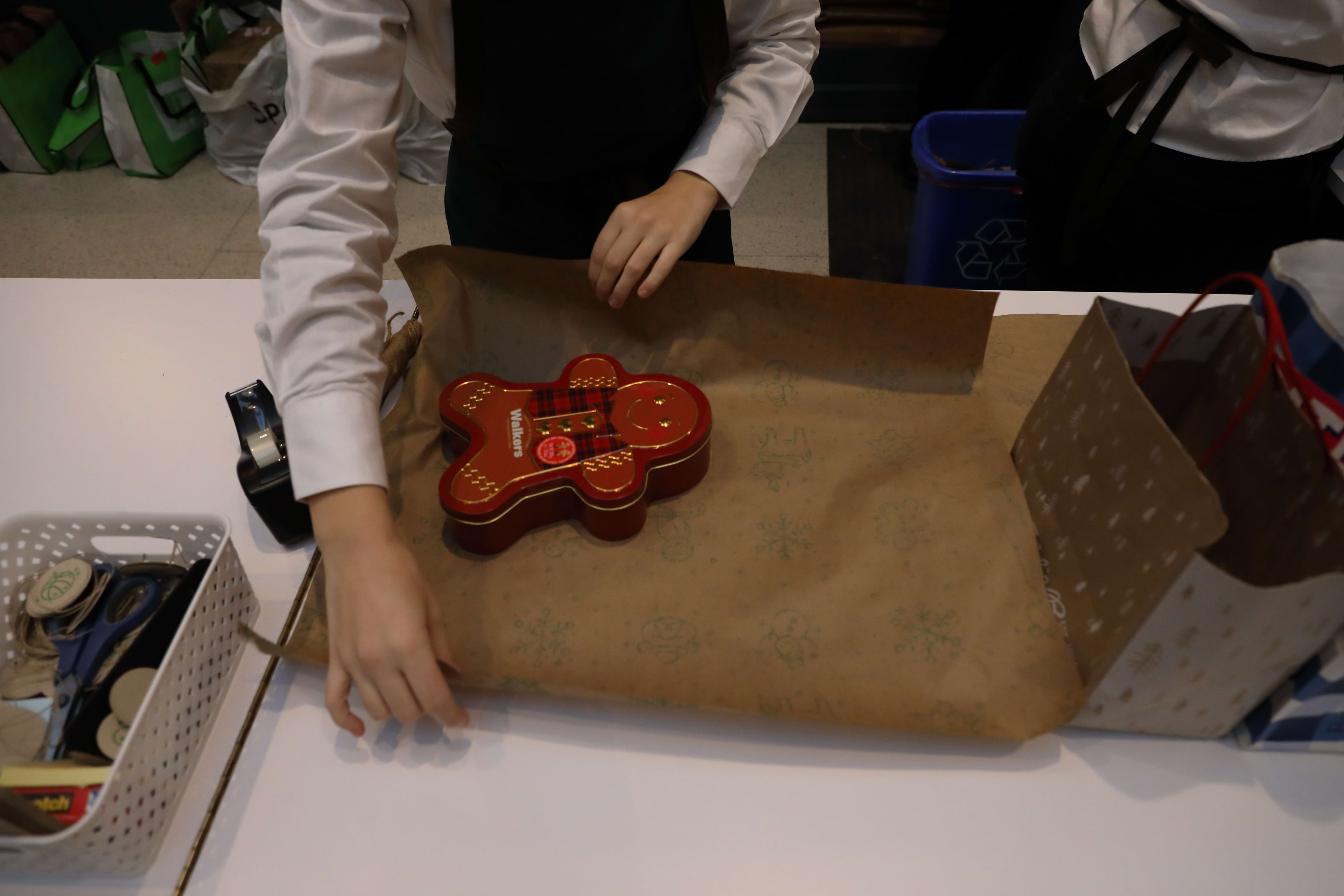 A woman gift wraps a gingerbread box.