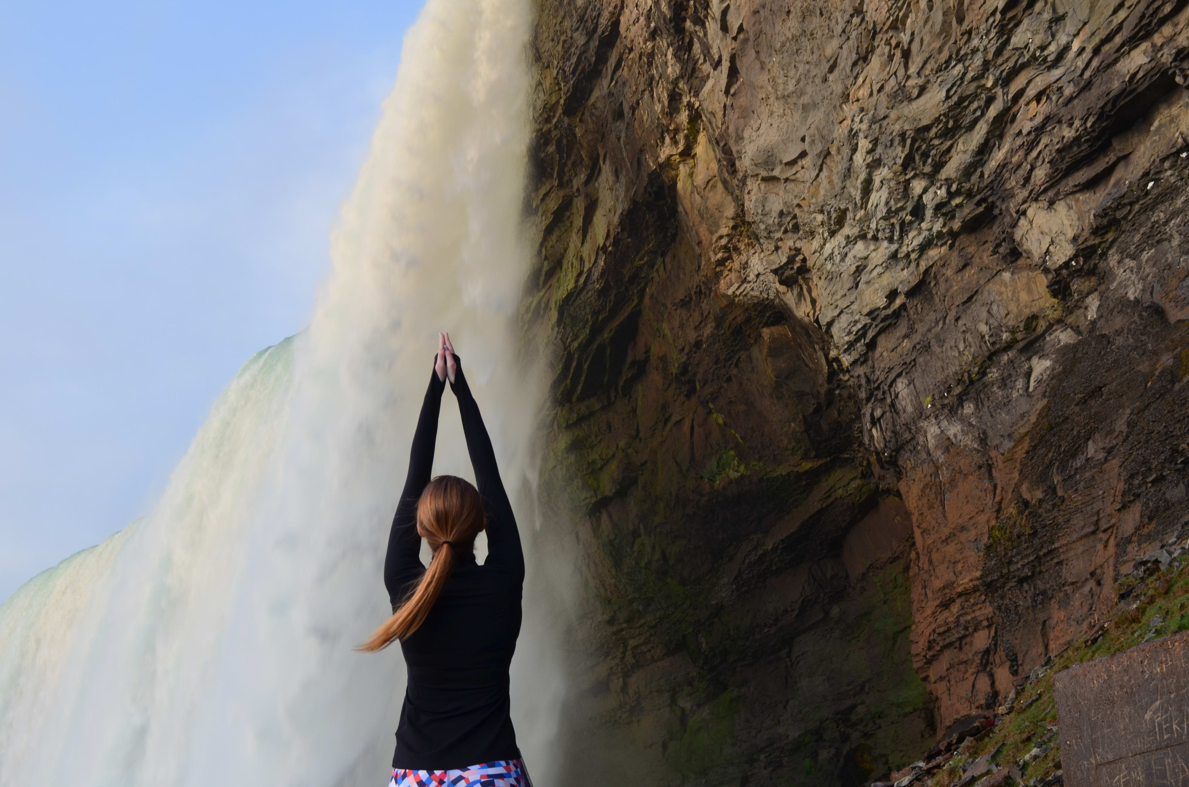 A woman holds a pose - hands high in the air - as the Falls pound nearby her.