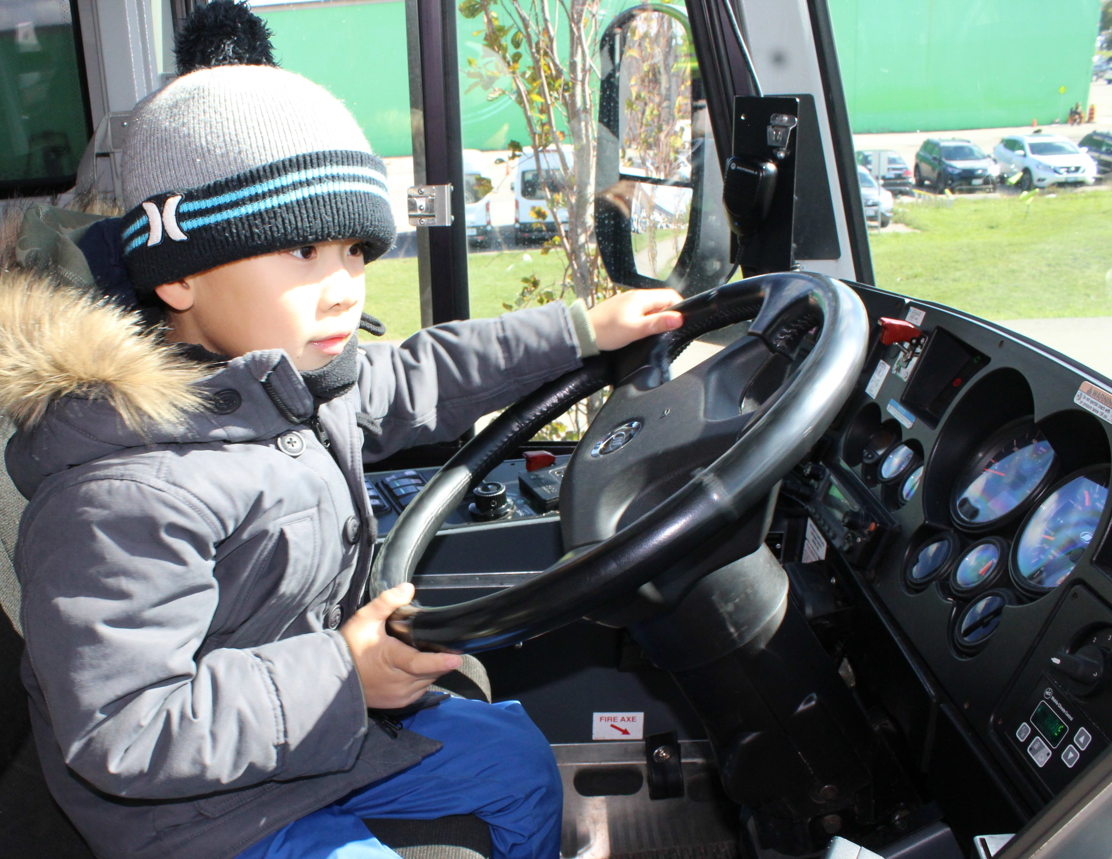 A young child steers the wheel of the GO bus.