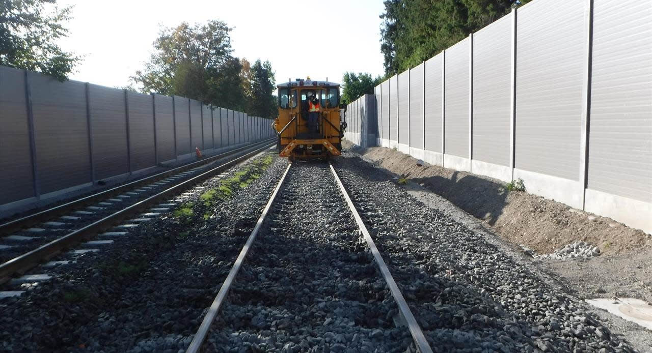 A maintenance vehicle moves along a new section of track with noise walls on either side