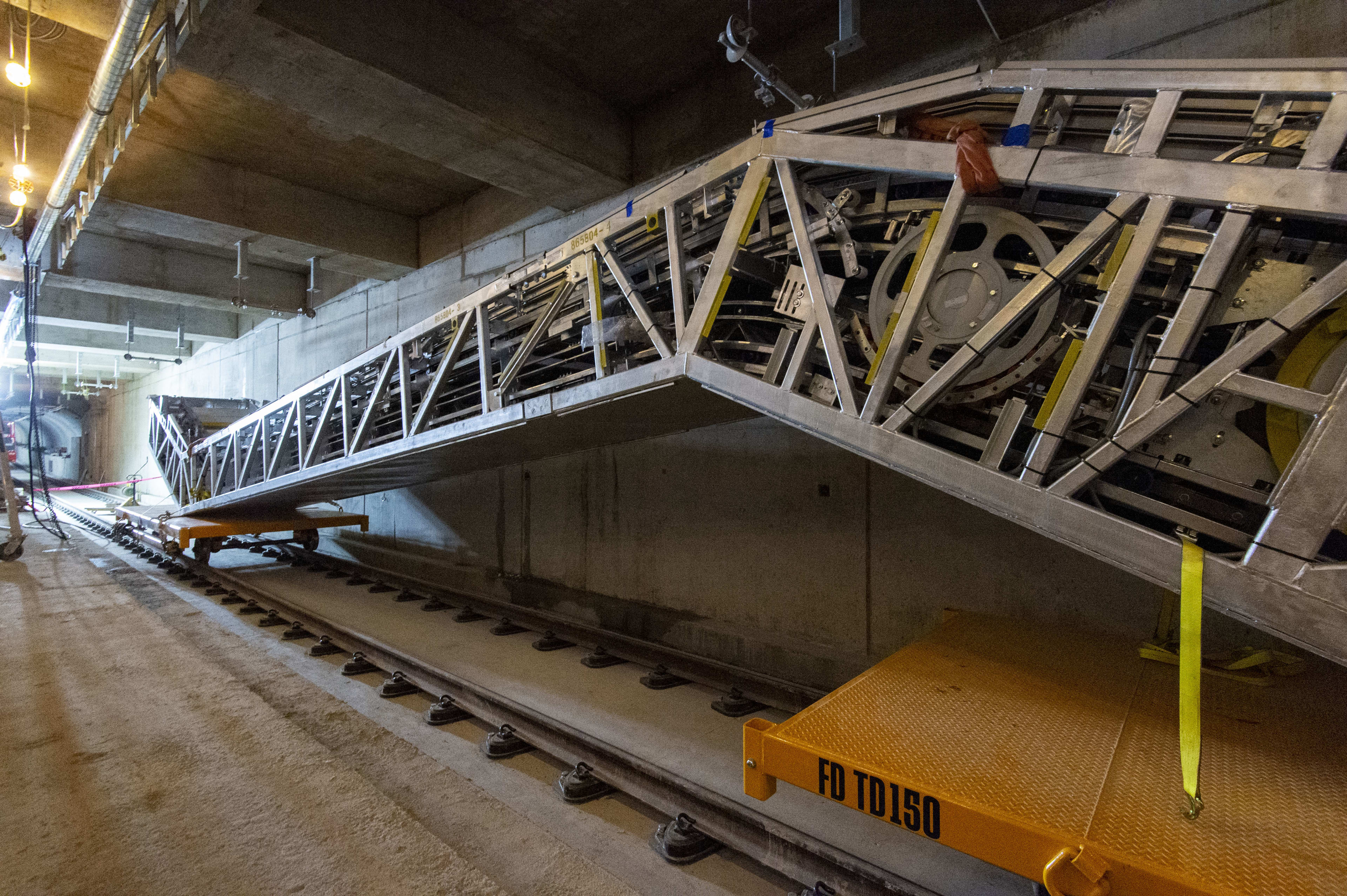A large escalator sits on two small rail cars, inside the LRT tunnel.