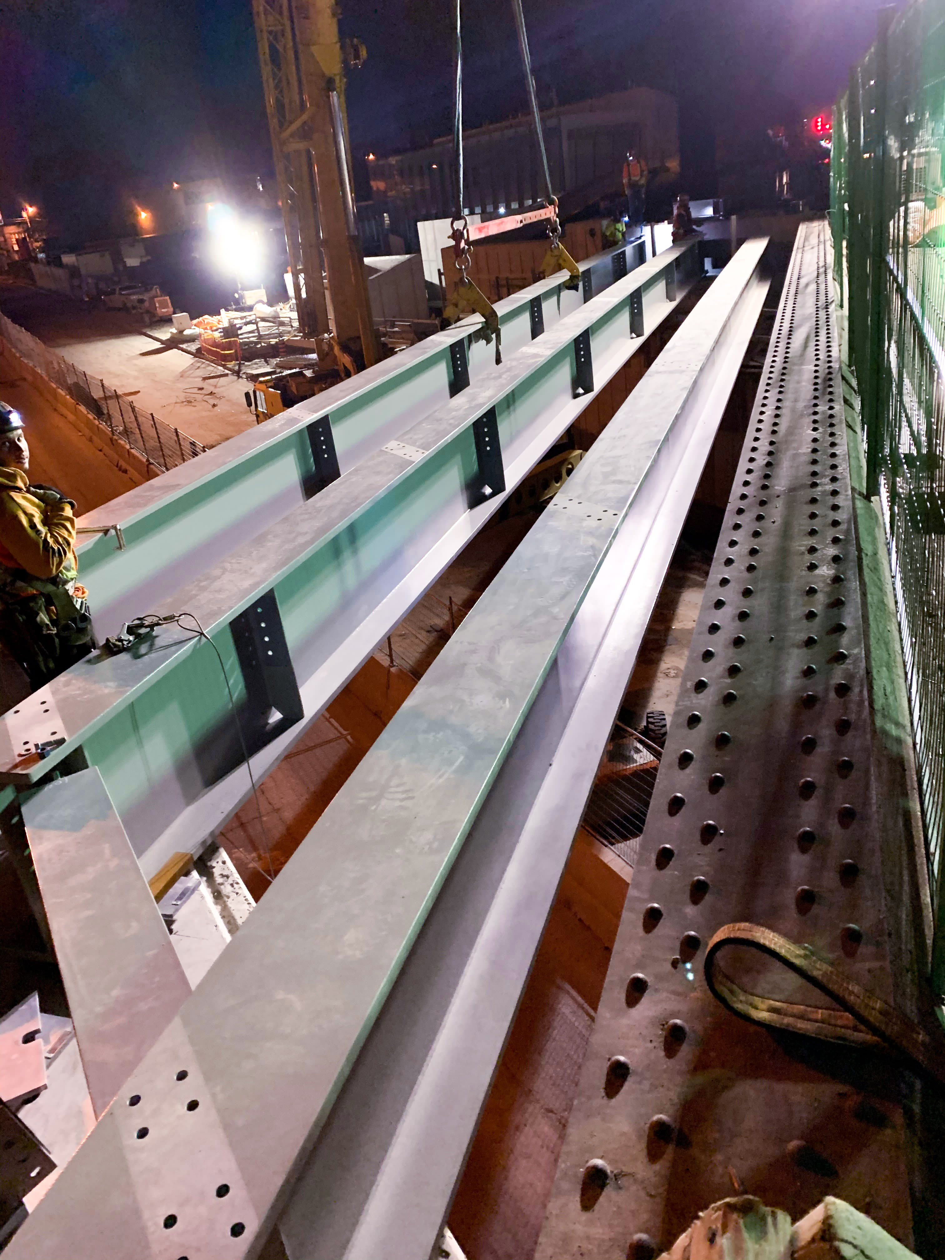 Workers put in large girders over a roadway.