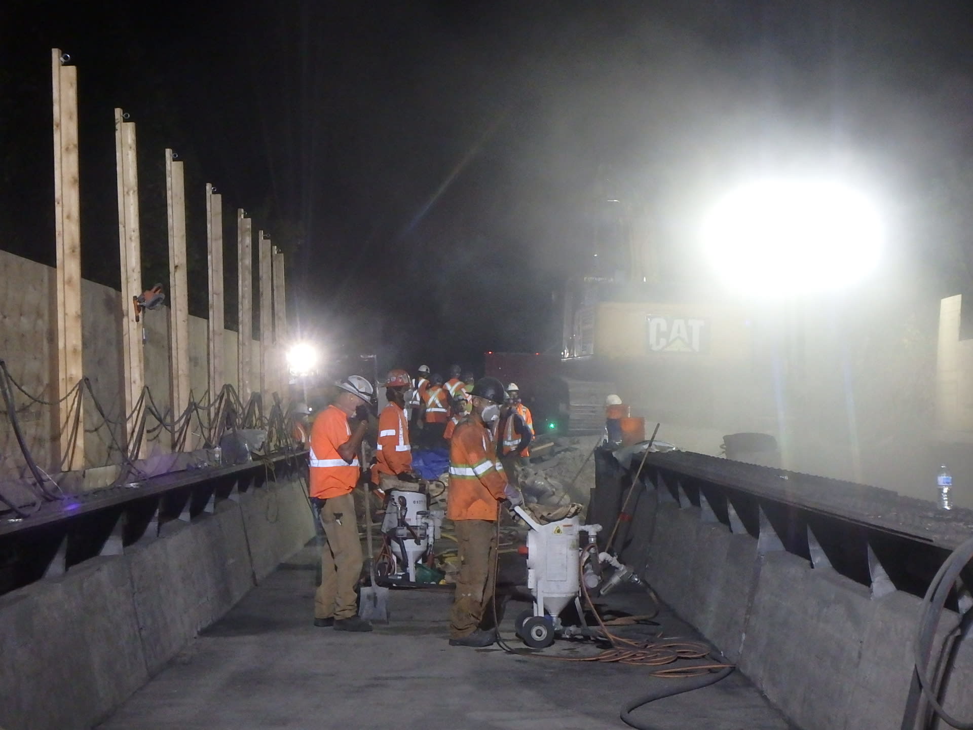 A night shot shows workmen sand blasting concrete on a bridge.