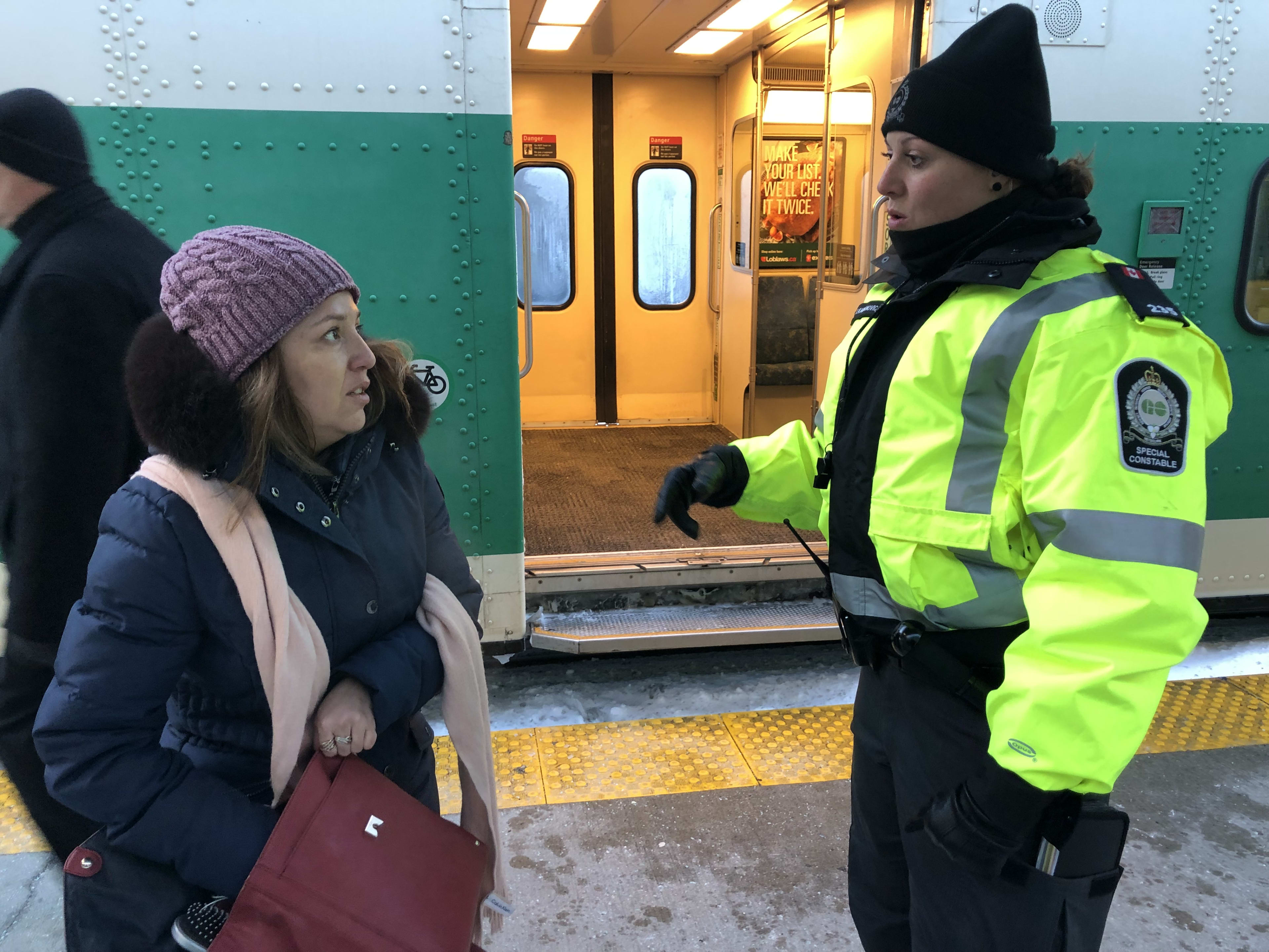 Officer Tihana Karanovic stands and speaks to a female passenger, who's looking through her purse...