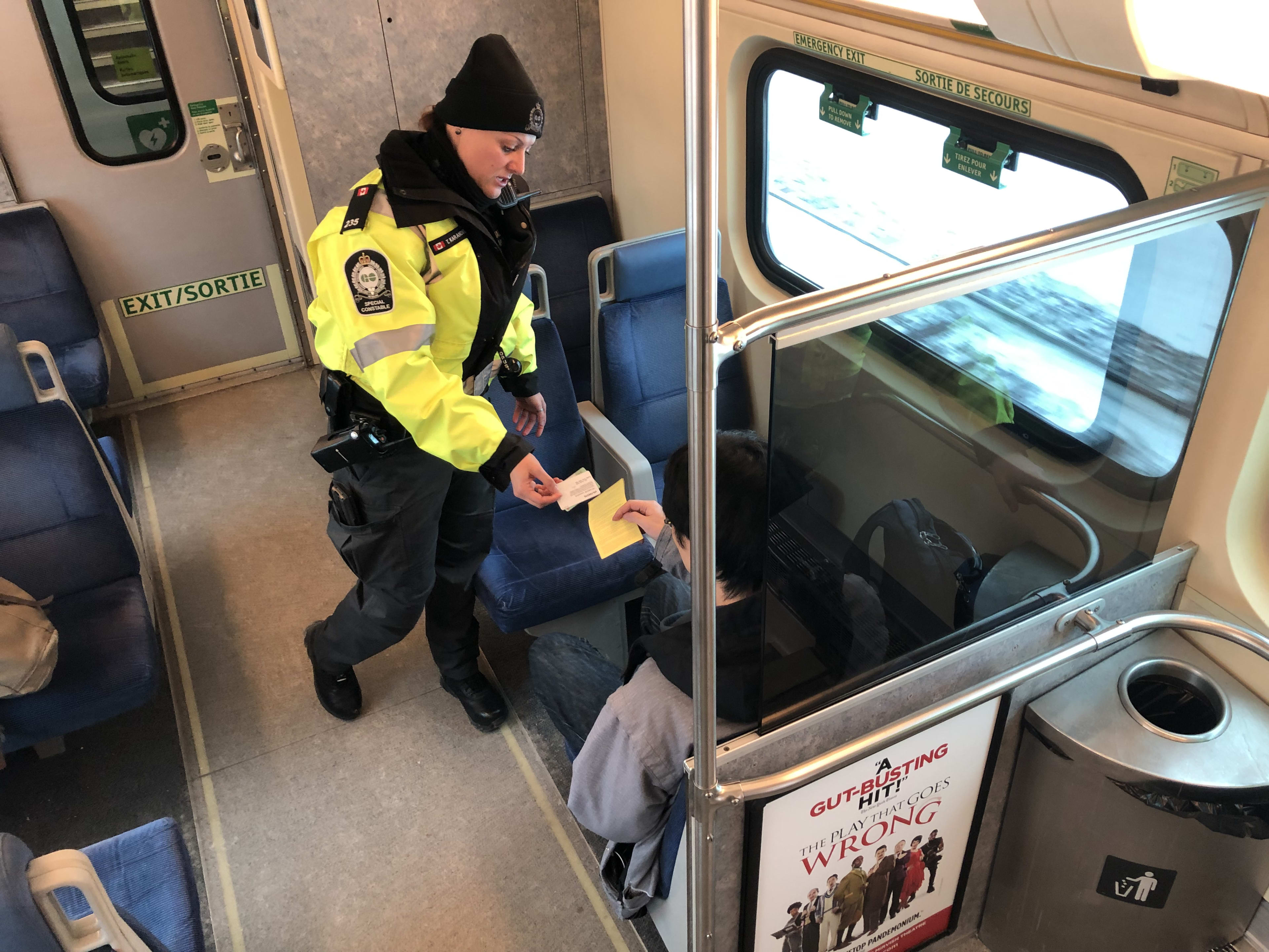 Officer Tihana Karanovic leans forward and hands a ticket to a seated passenger.