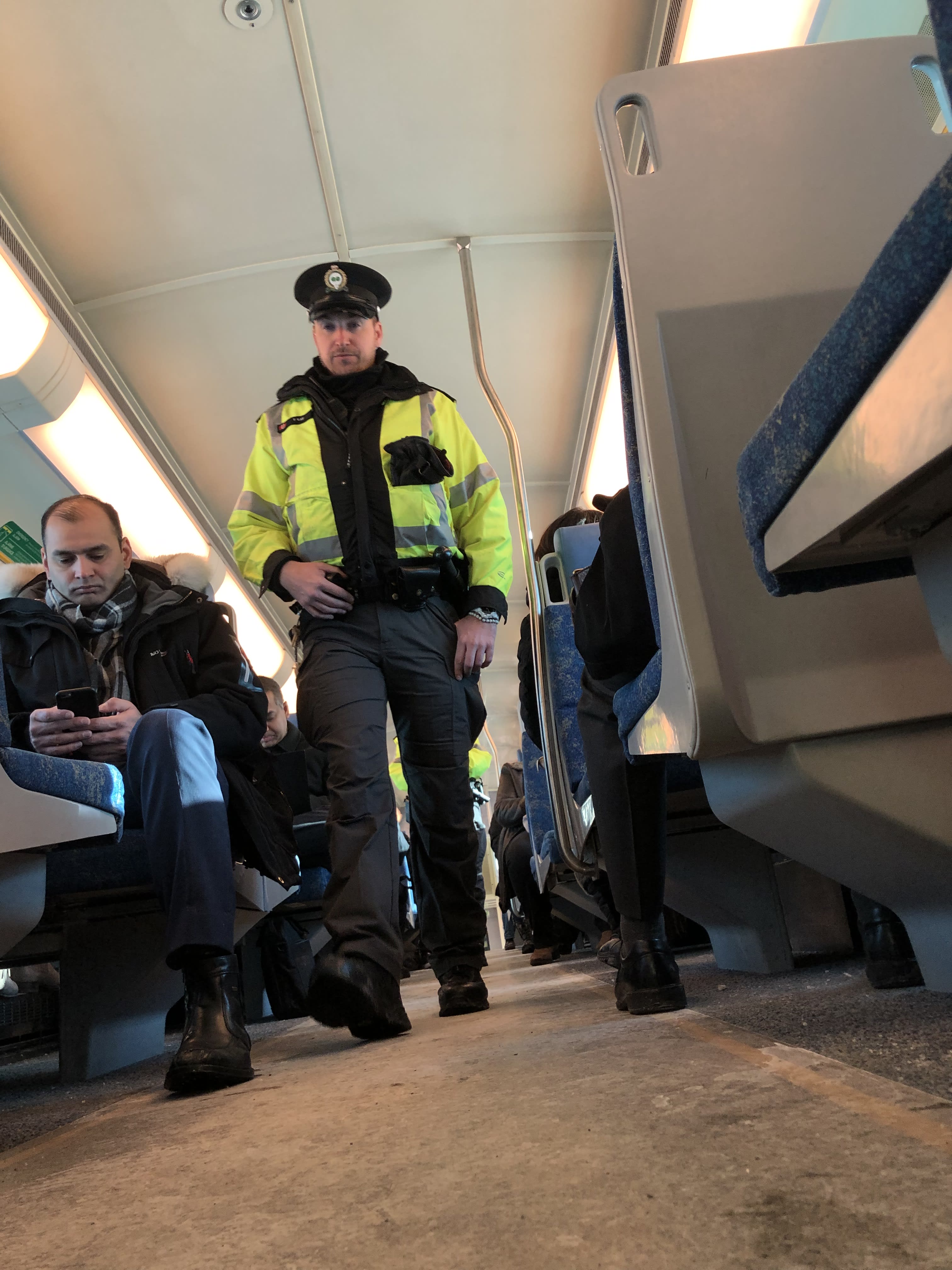 Officer Tyler Kay walks through a partially filled train. The shot is at ground level.