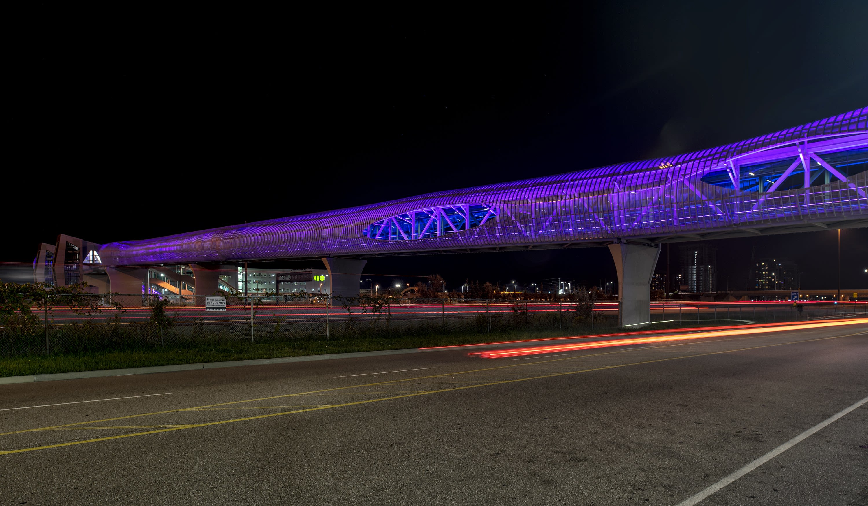 The Pickering pedestrian bridge is shown lit up in blue at night, as it stands over busy Hwy. 401.