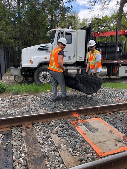 workers carry an anti-trespass mat from a truck to the train tracks.