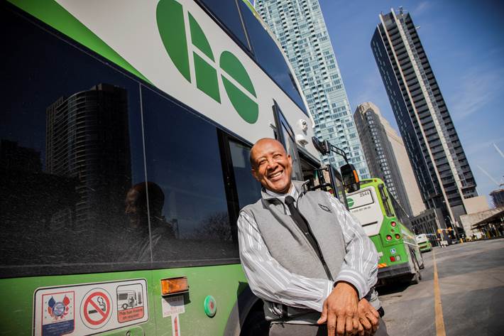 In this image from March 2019, Derrick Sealy stands outside his bus on a sunny day, smiling at th...