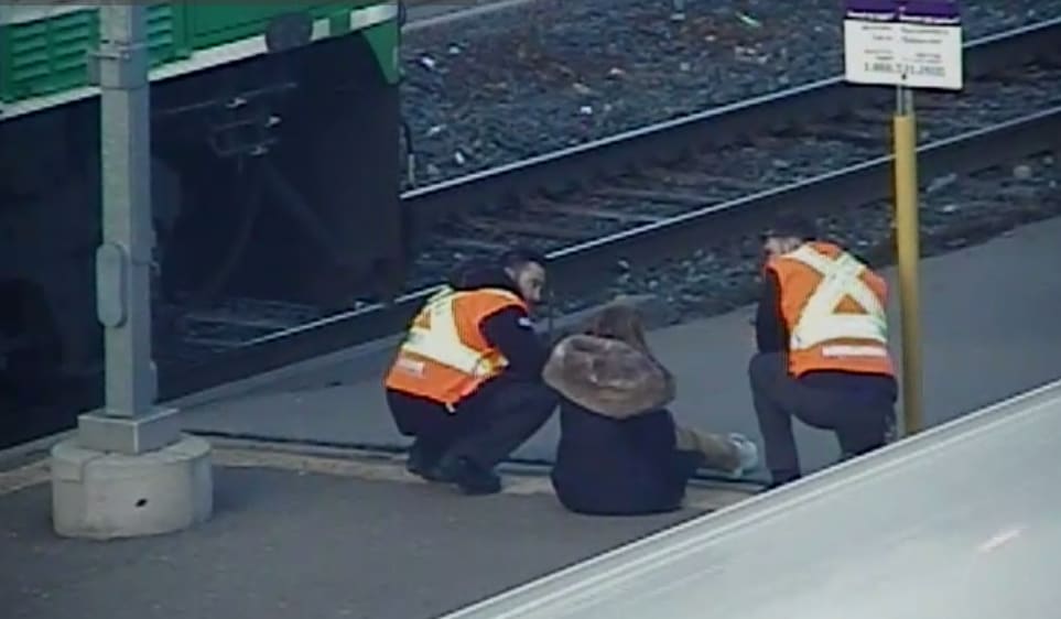 Two staff members talk to a young woman on a train platform.