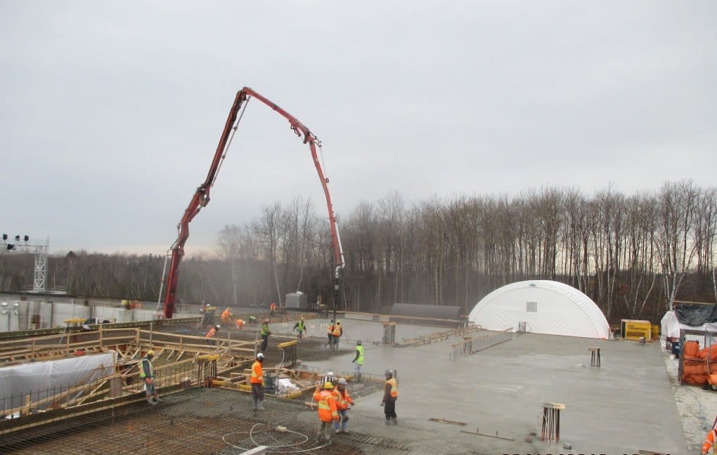 Men and equipment pour grey concrete onto the construction site.