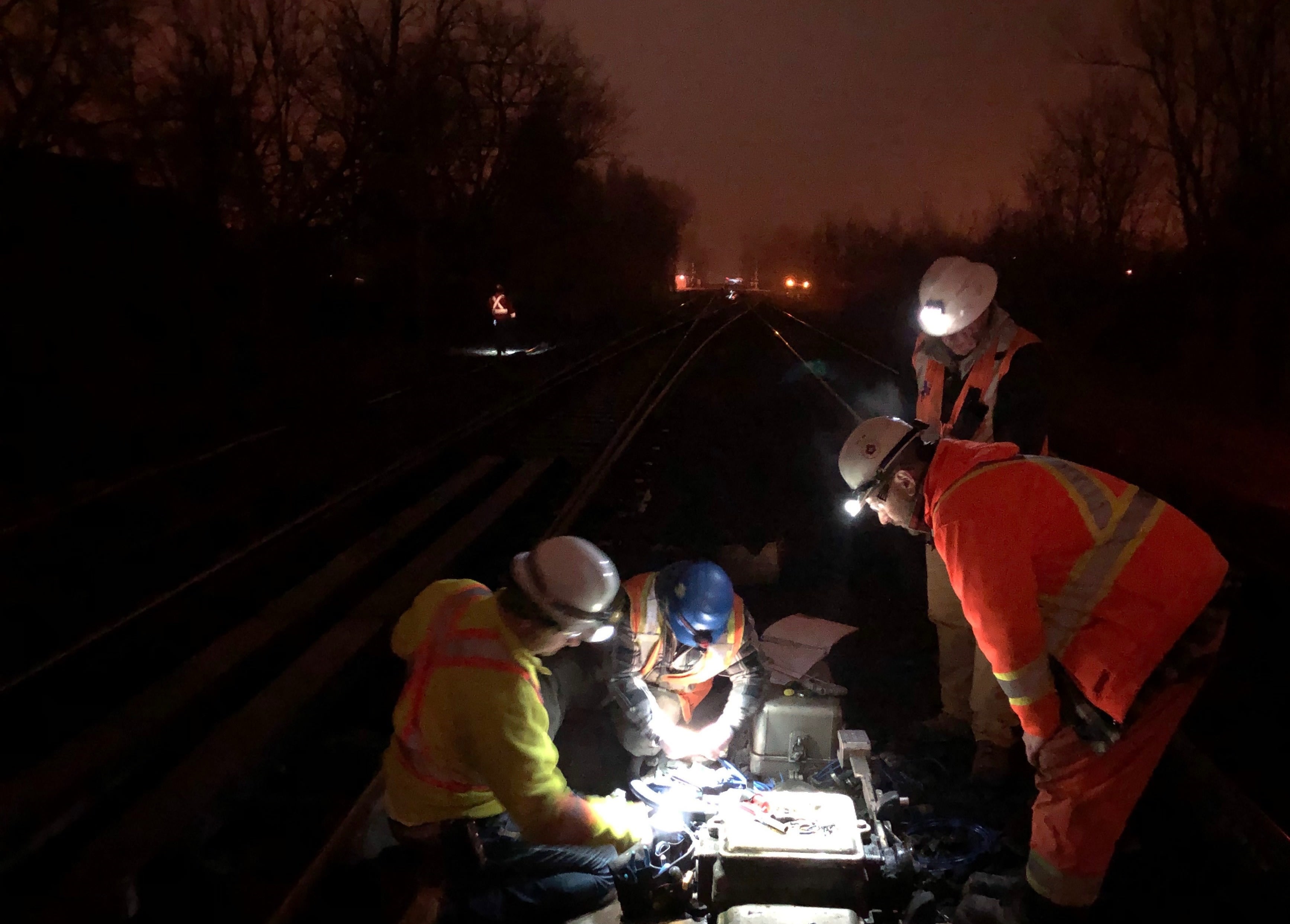 Four workmen toil away in the dark, as they peer into a piece of rail equipment.