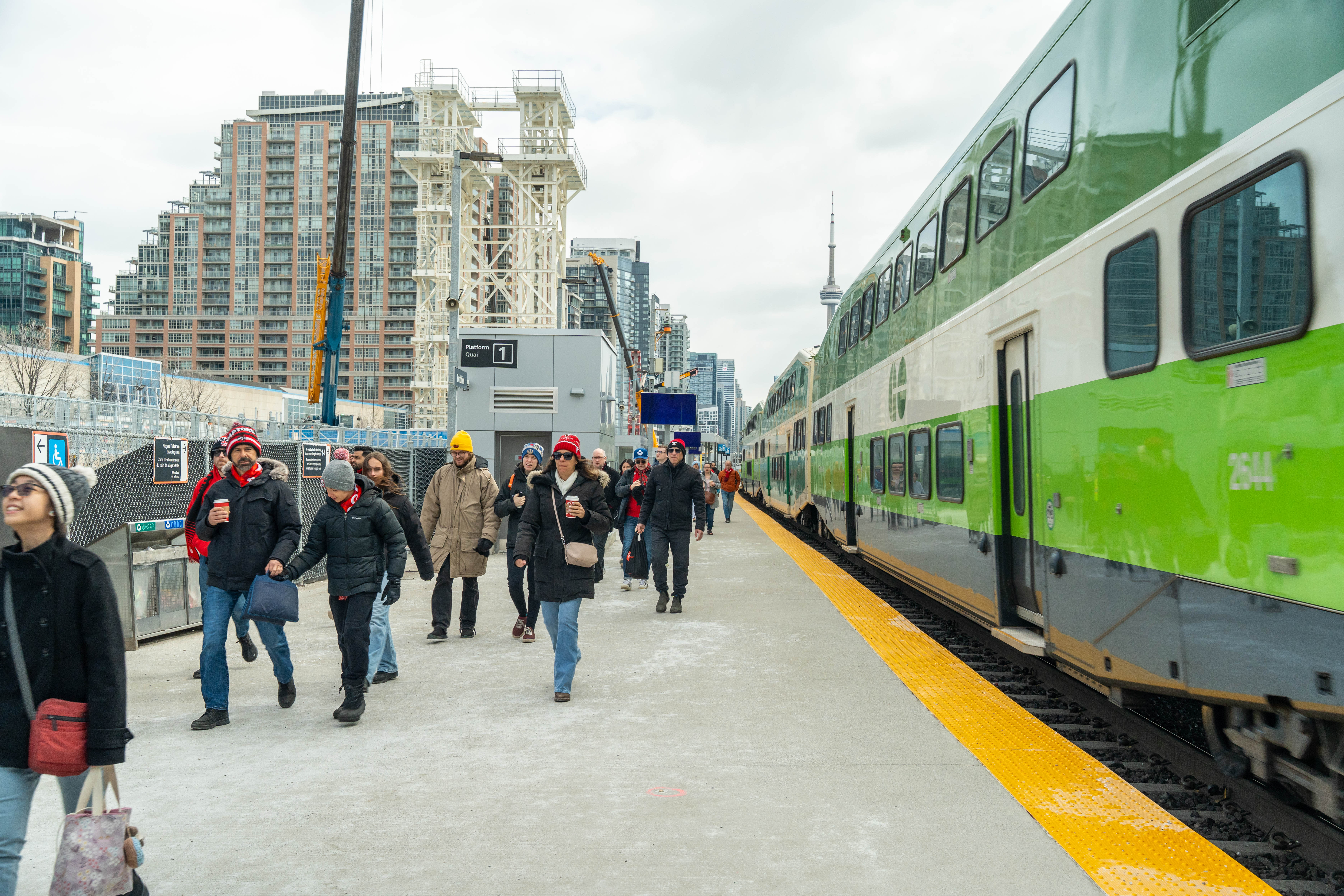 Passengers walking beside a GO train with the CN Tower visible in the background.