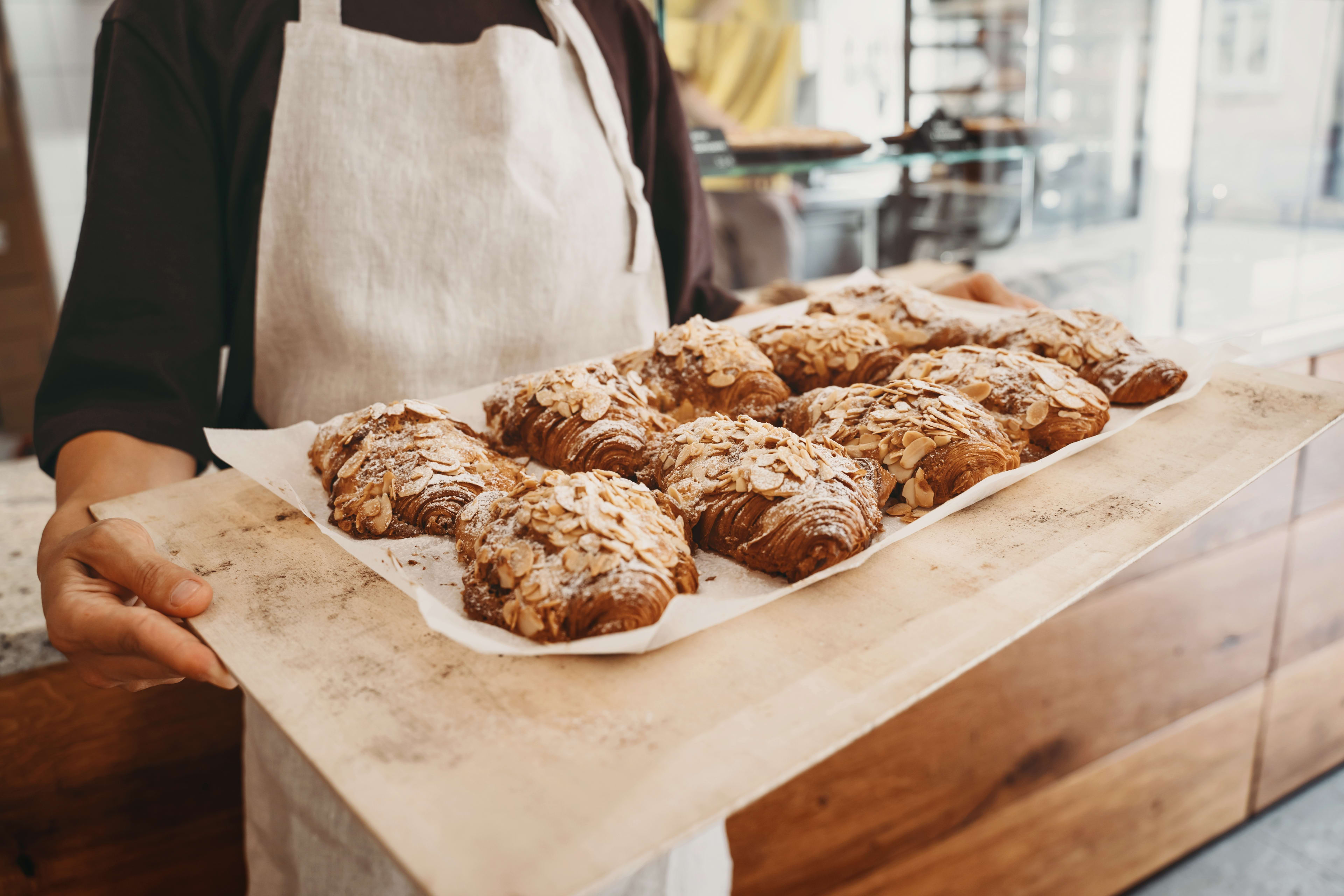 Baker holding tray of almond croissants