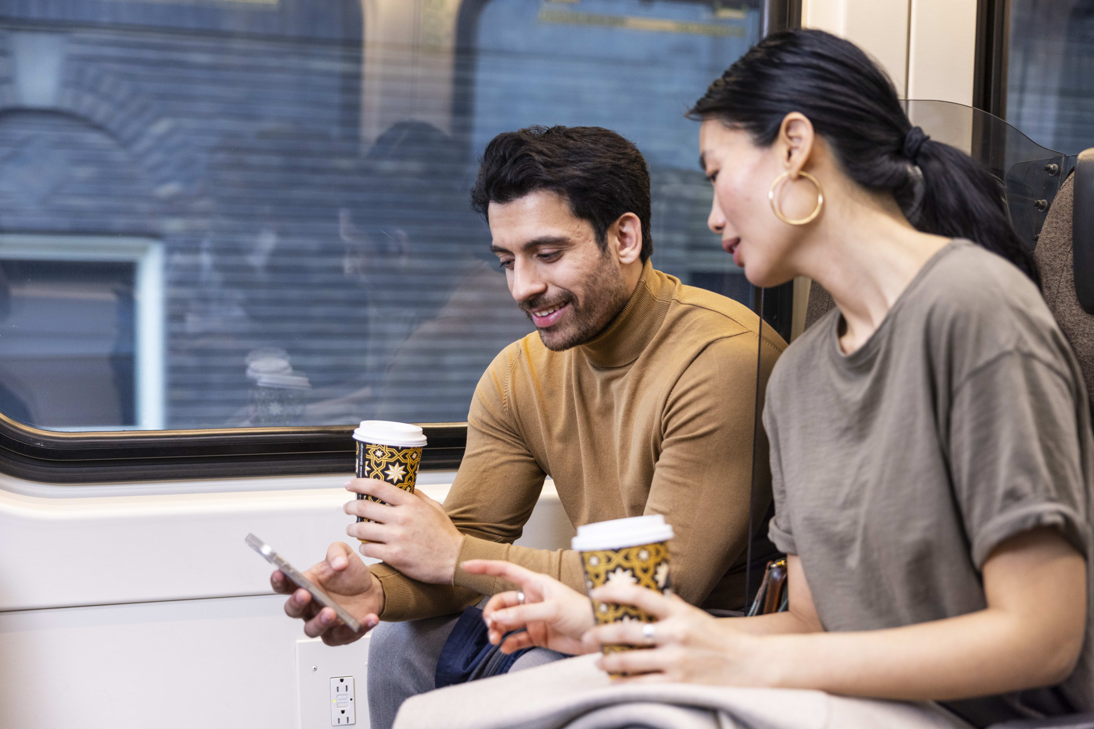 Two people sitting on board UP Express looking at phone holding coffee cups