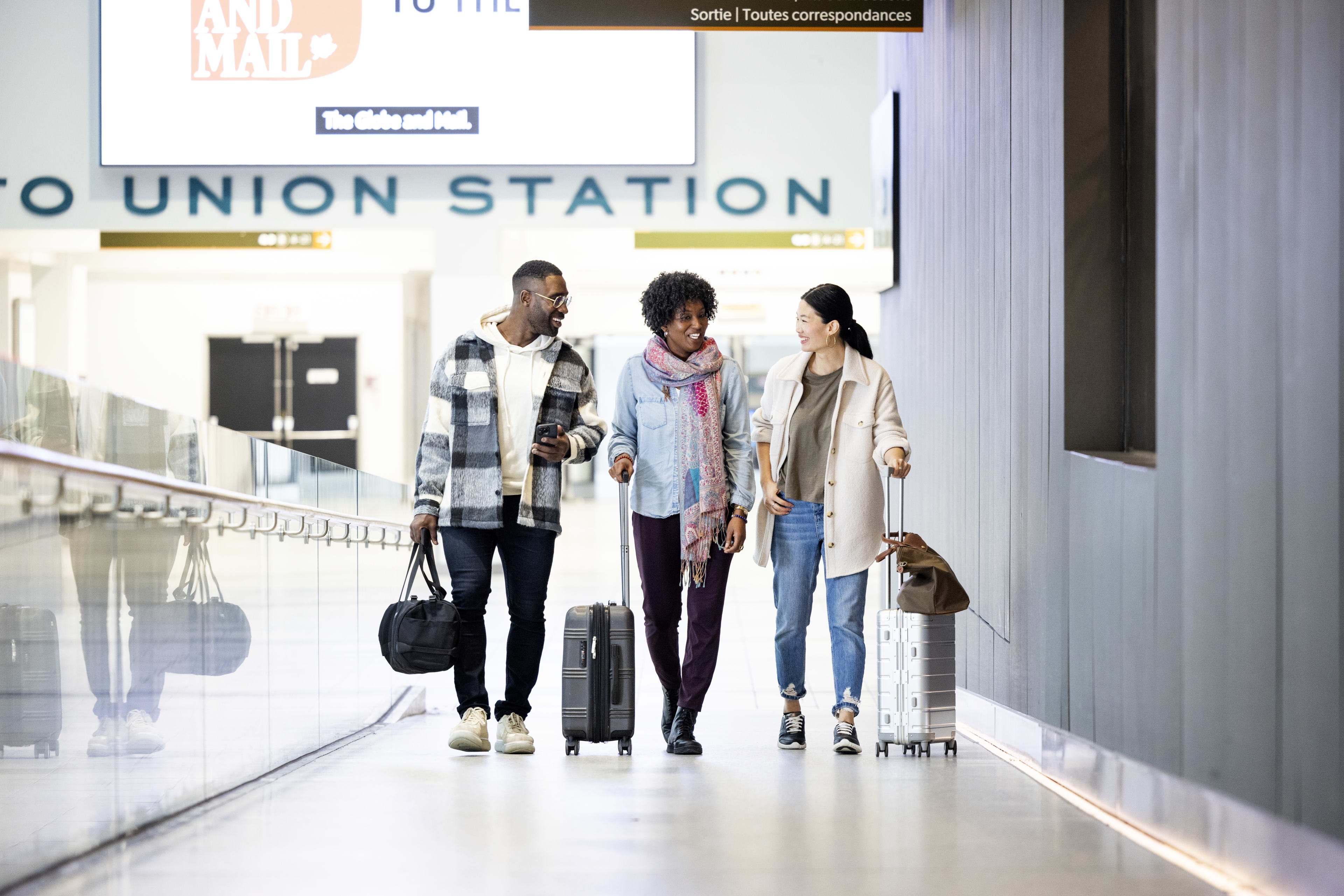 Three adults walking up the ramp towards the entrance of UP Union Station with bags and luggage.