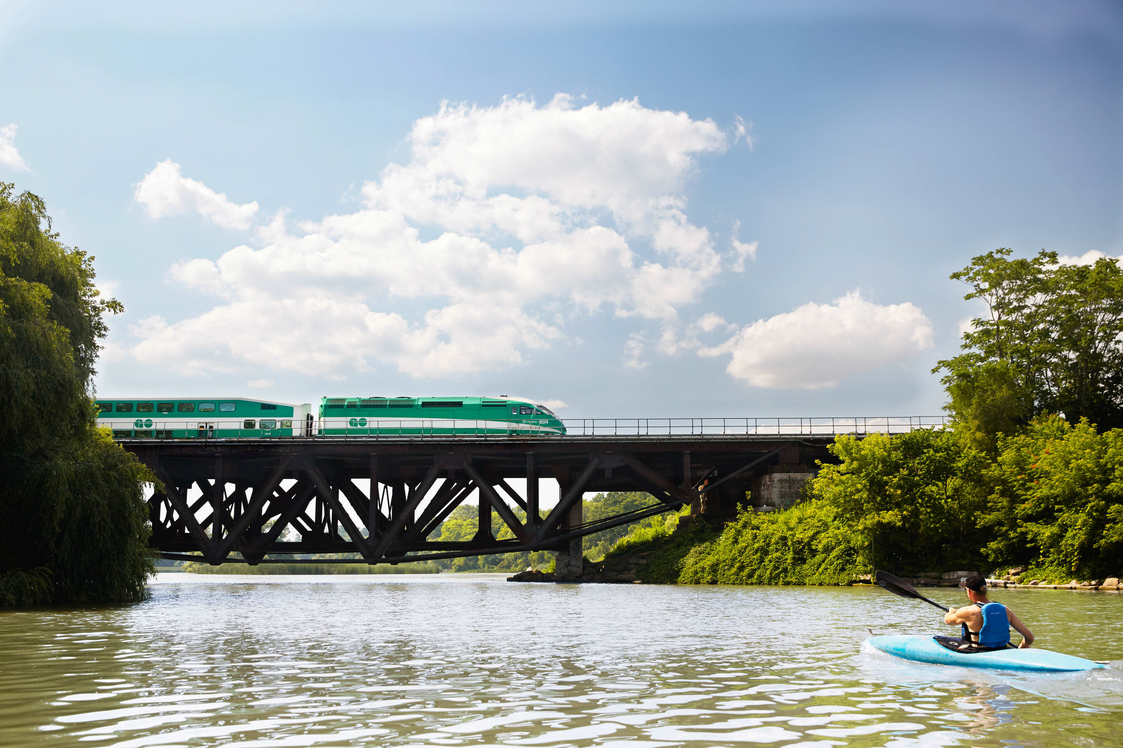 GO Train travelling across a bridge in the summer