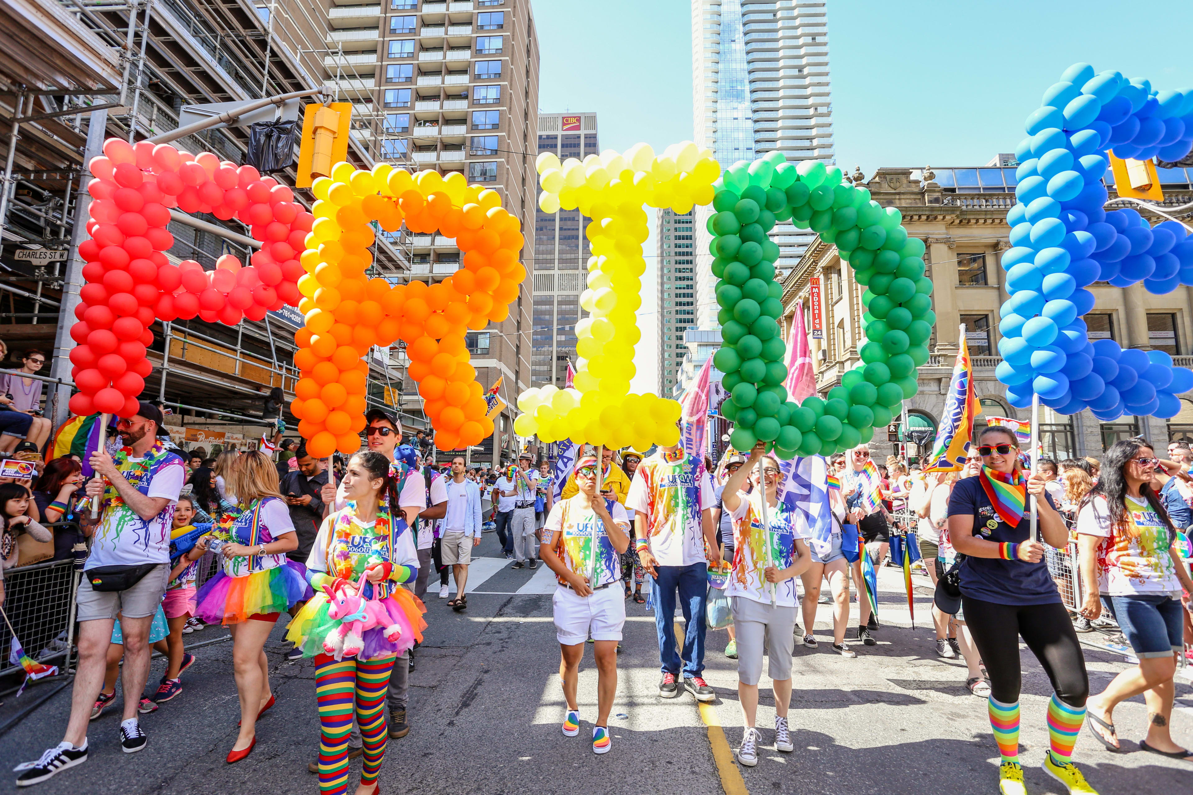 A group of people walking in Pride Parade, holding up balloons that spell PRIDE.