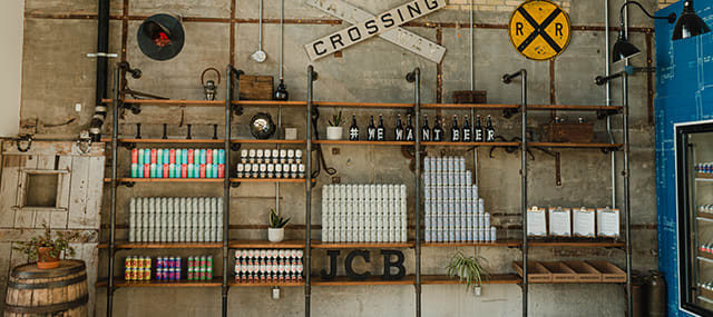 Brick wall with shelfs containing various beer cans, beer bottles and rail crossing signs.