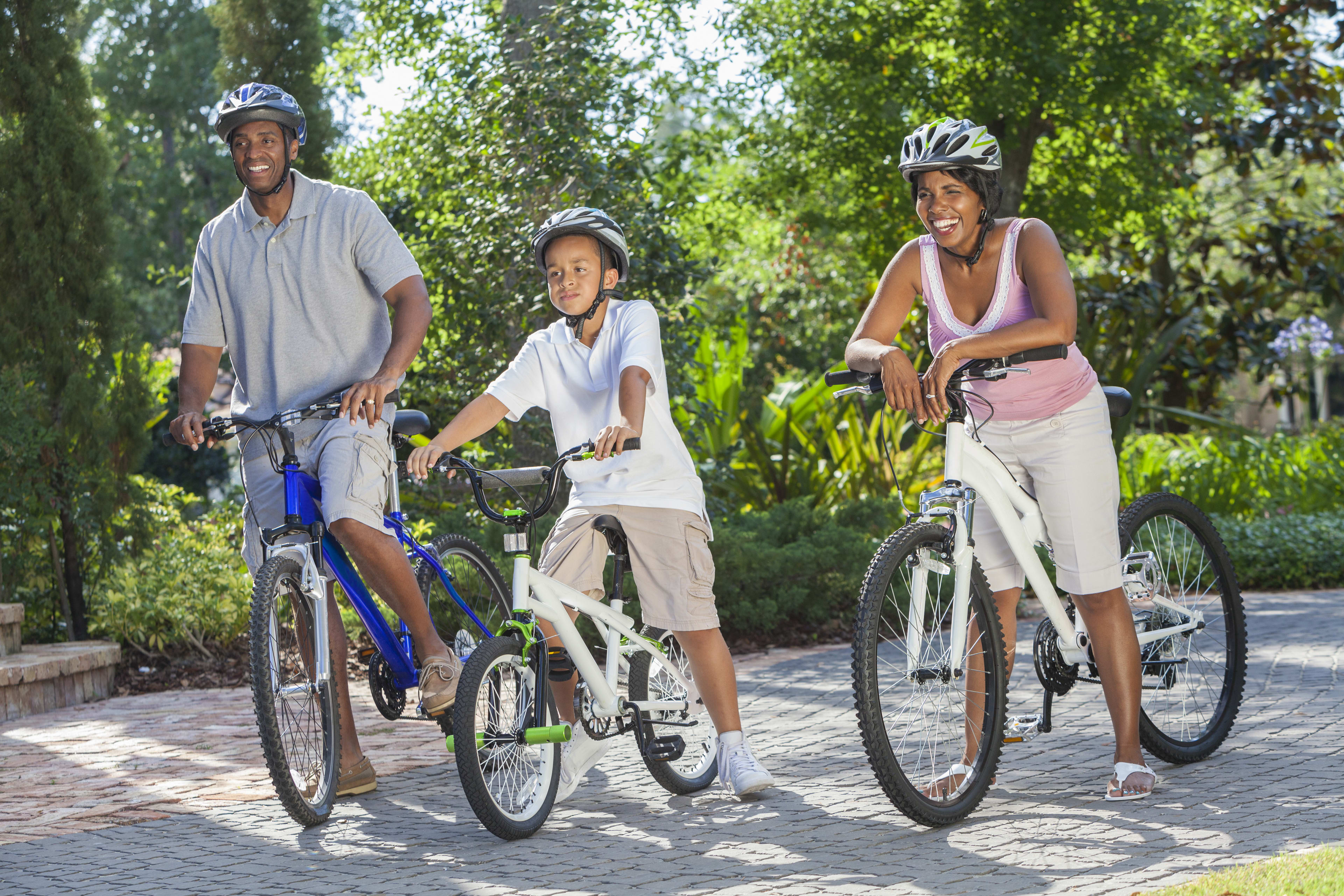 Family of three on bikes riding down paved path surrounded by trees