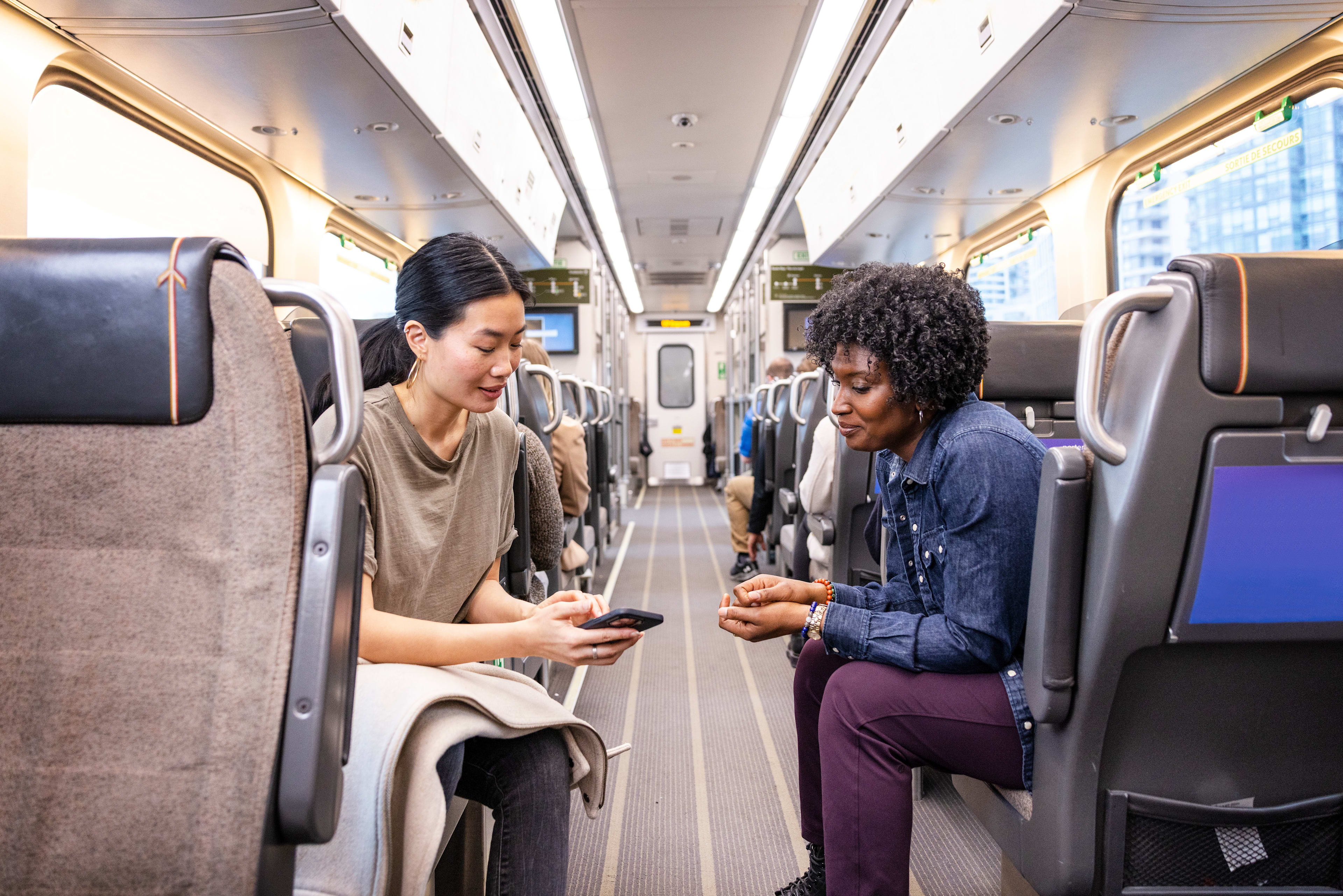 Two women onboard UP Express looking at a phone.