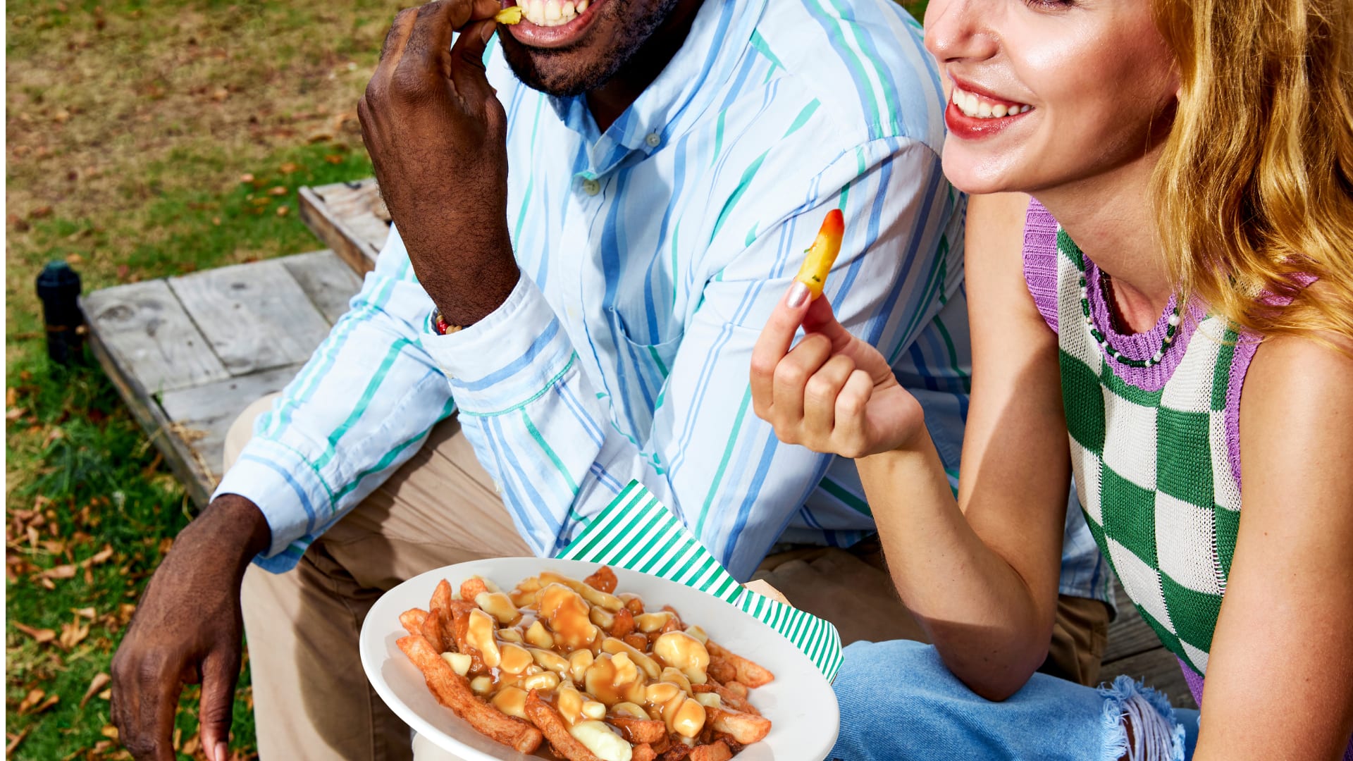 Two people sitting on the ground eating poutine