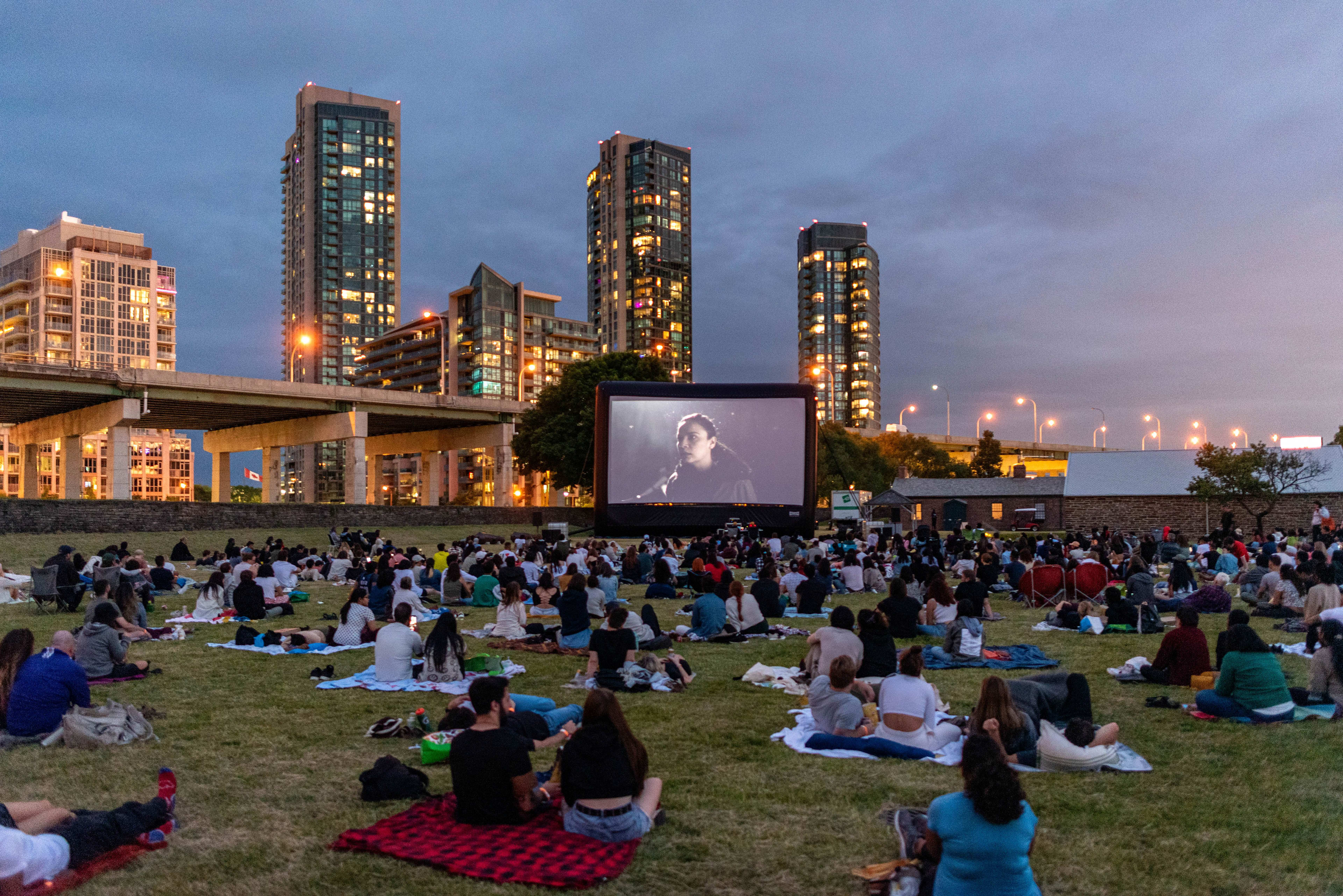Toronto Outdoor Picture Show playing a movie with people sitting outdoors on blankets watching