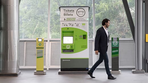 A passenger in a station walks past a ticketing machine and 2 Presto card machines.