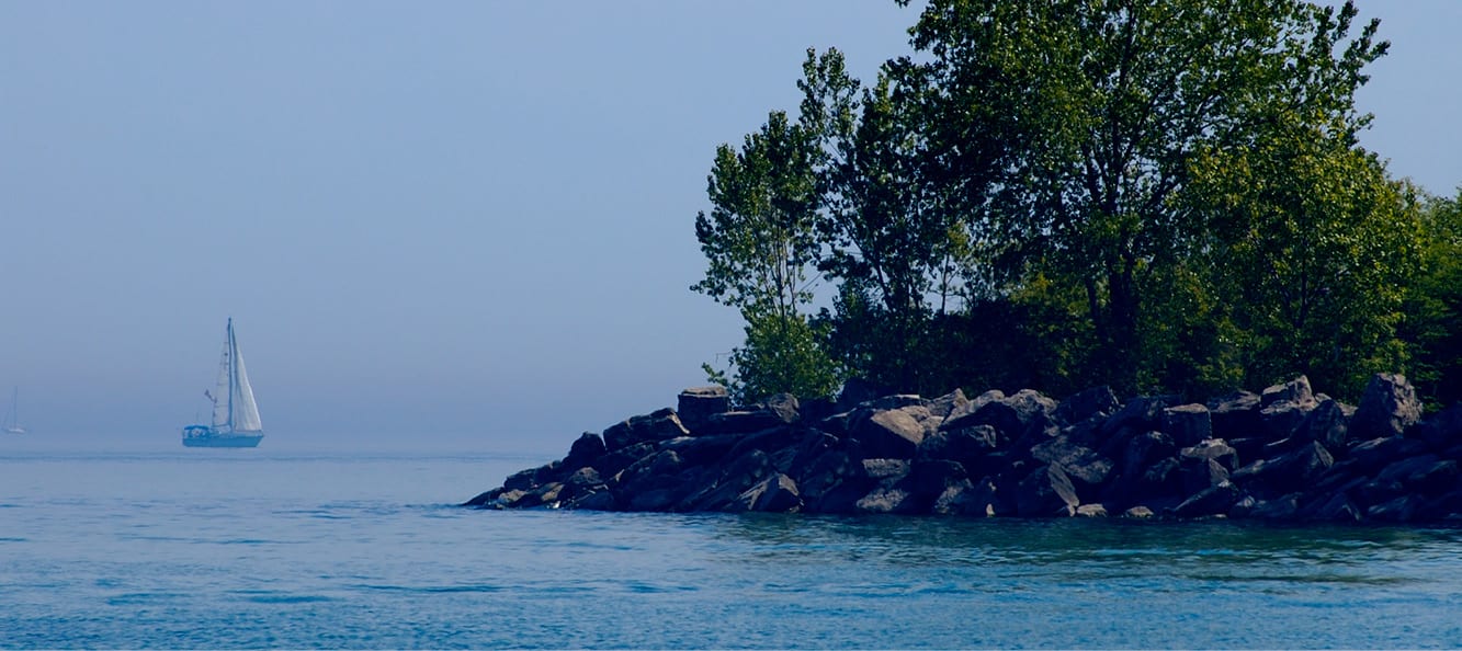 Small island in a lake built with rocks and trees on top with sail boat to the left