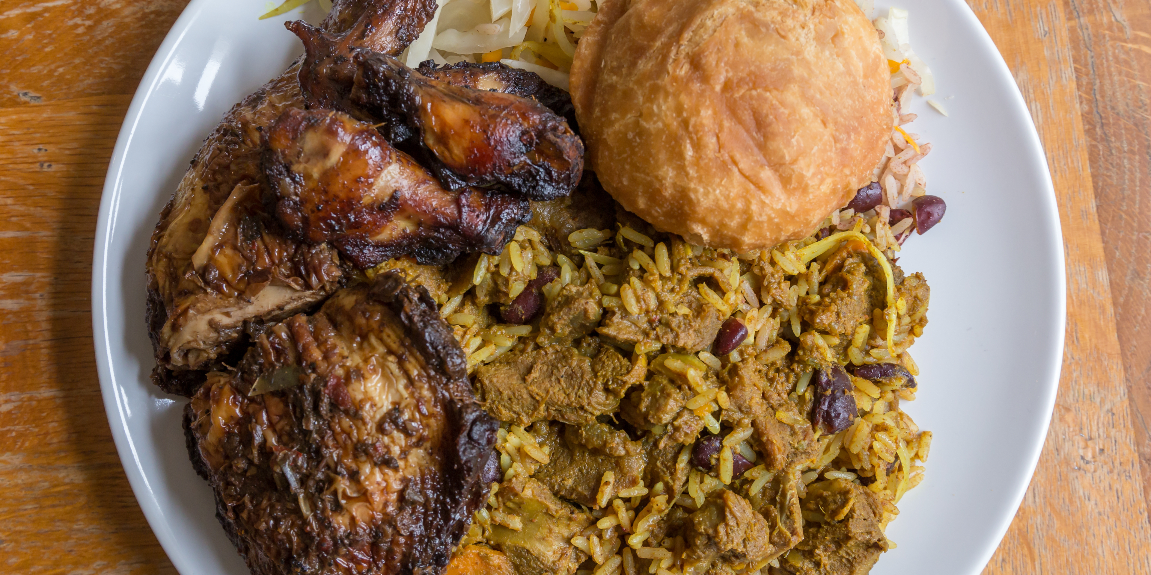 Plate of jerk chicken, curry rice and a sandwich