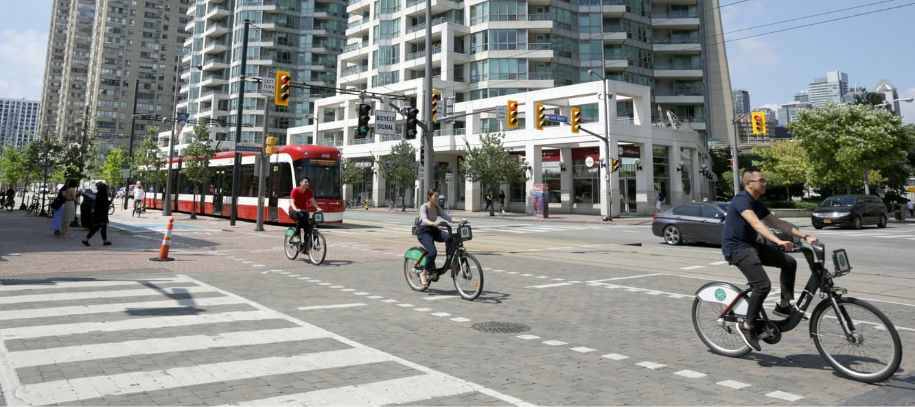 Toronto Queen's Quay during day with three people riding bicycles in a bike lane.