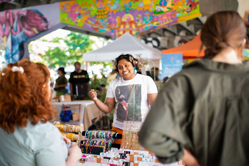 Person at booth with table with jewelery smiling talking to other people