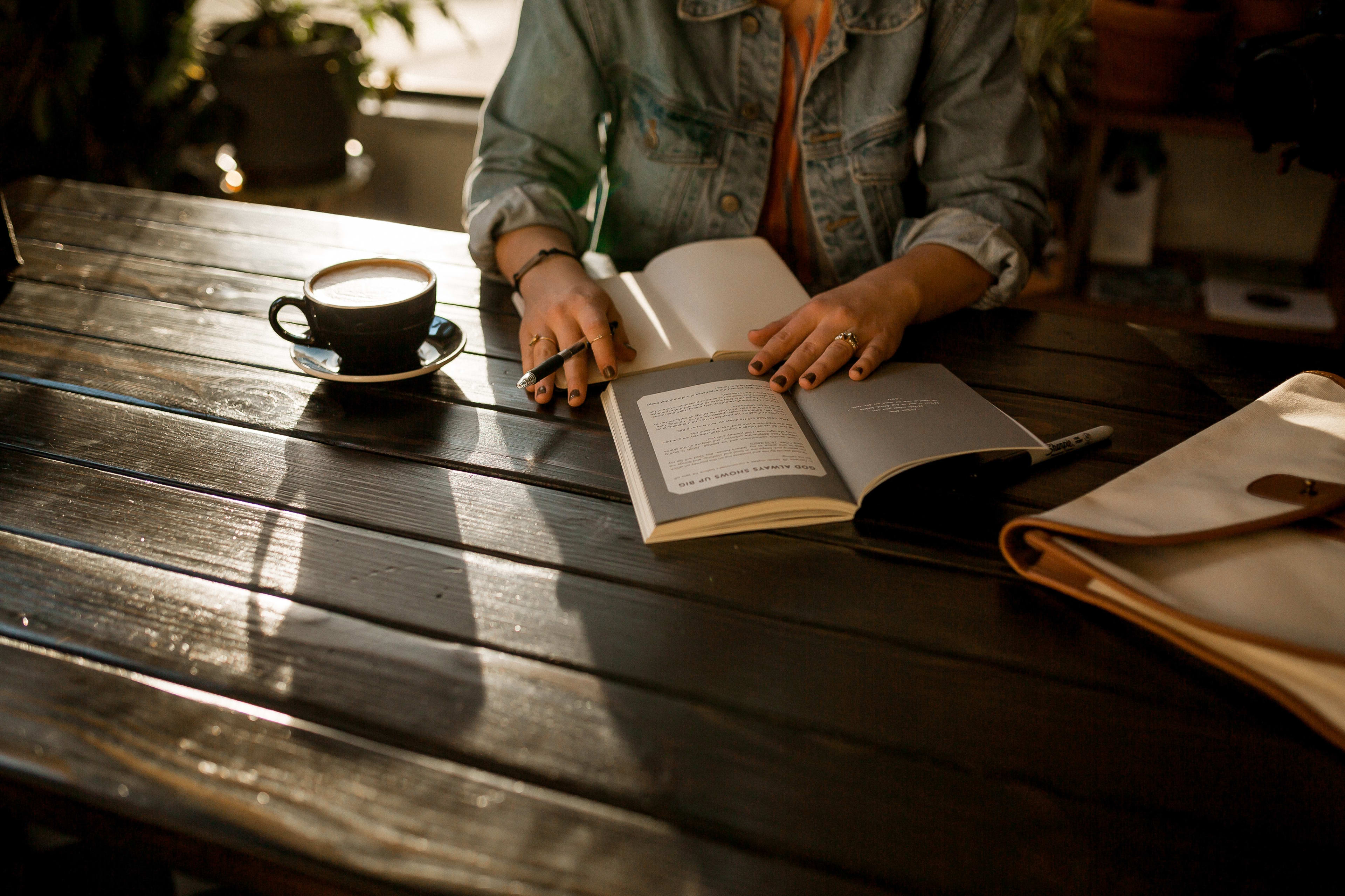 Person sitting at table, reading book with a cup of coffee