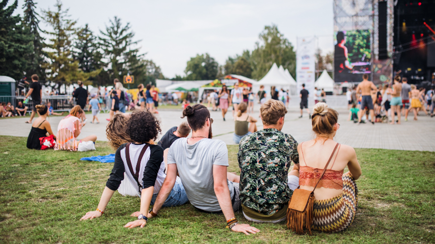 Group of people sitting on the ground at an outdoor music festival watching the stage