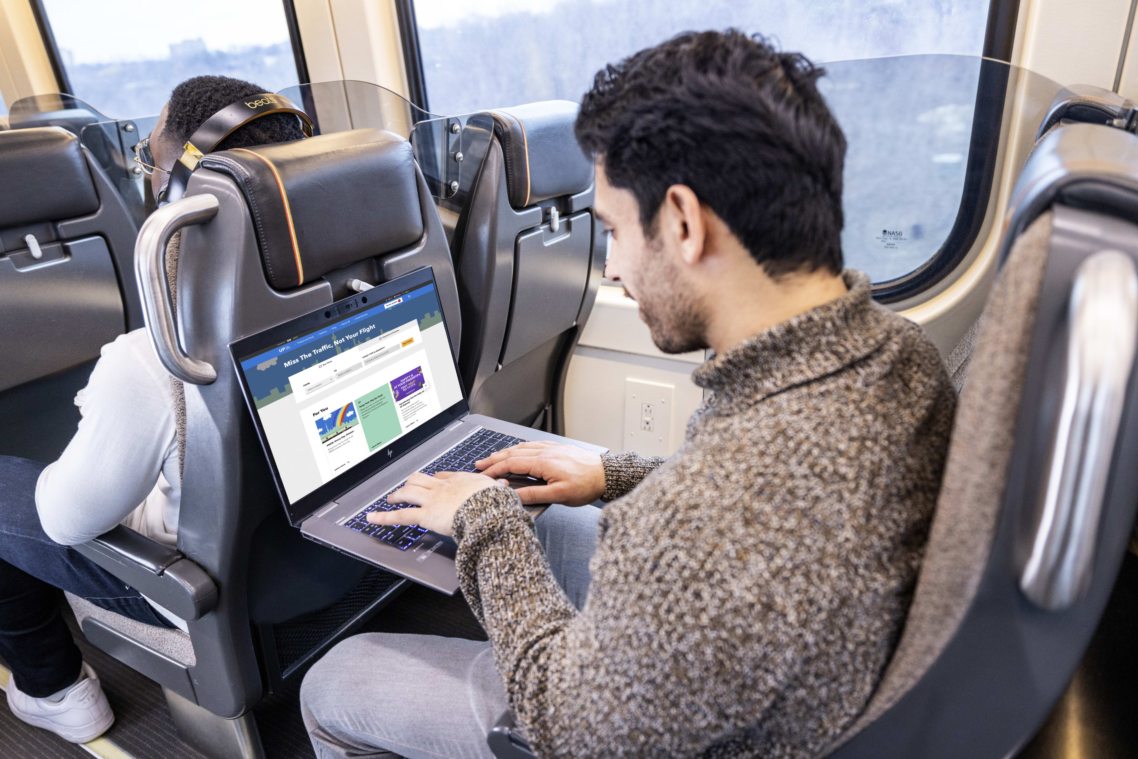Man sitting onboard train on computer browsing UP website on a laptop