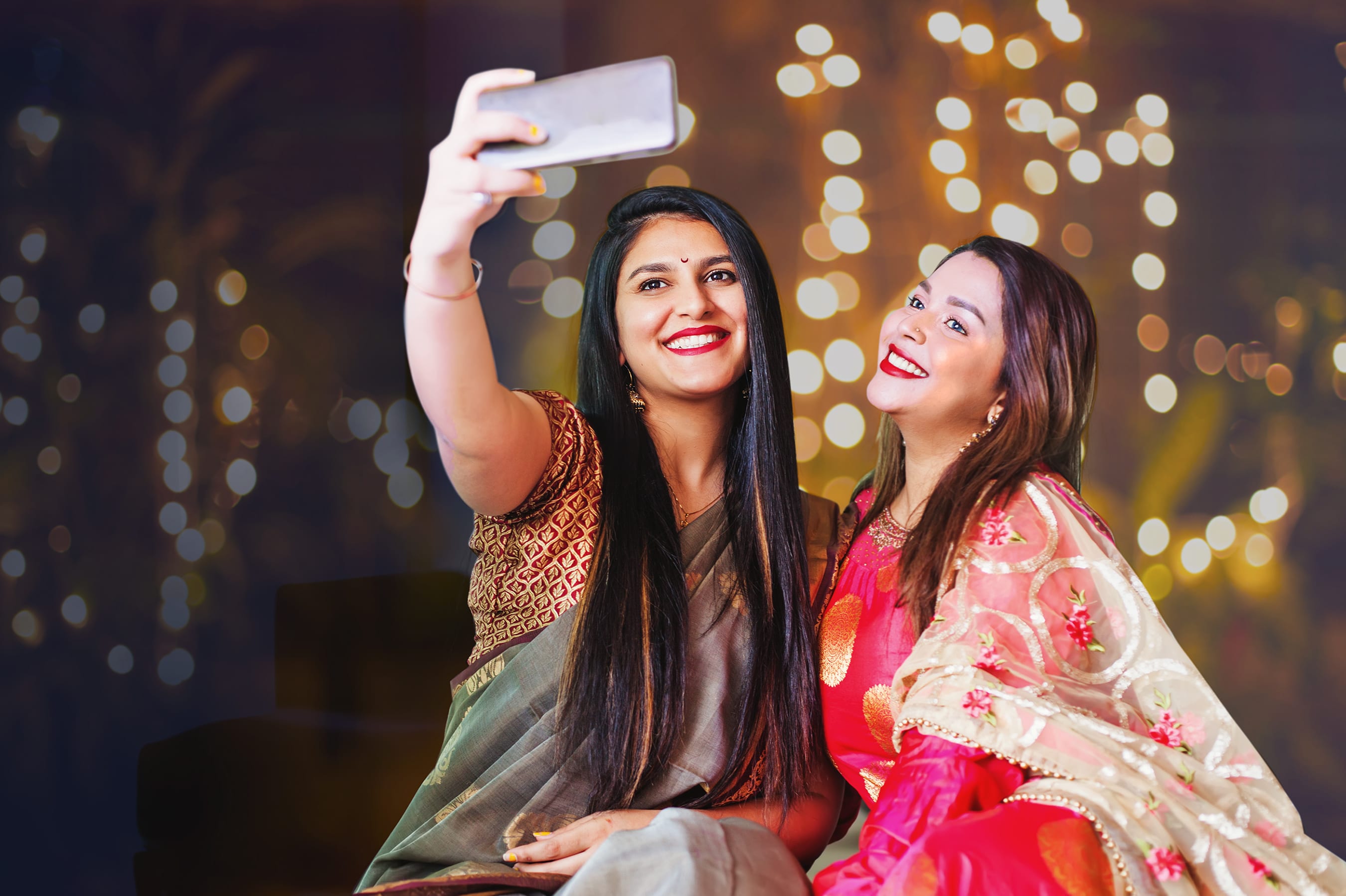Two ladies sitting, dressed up for Diwali party, taking a selfie