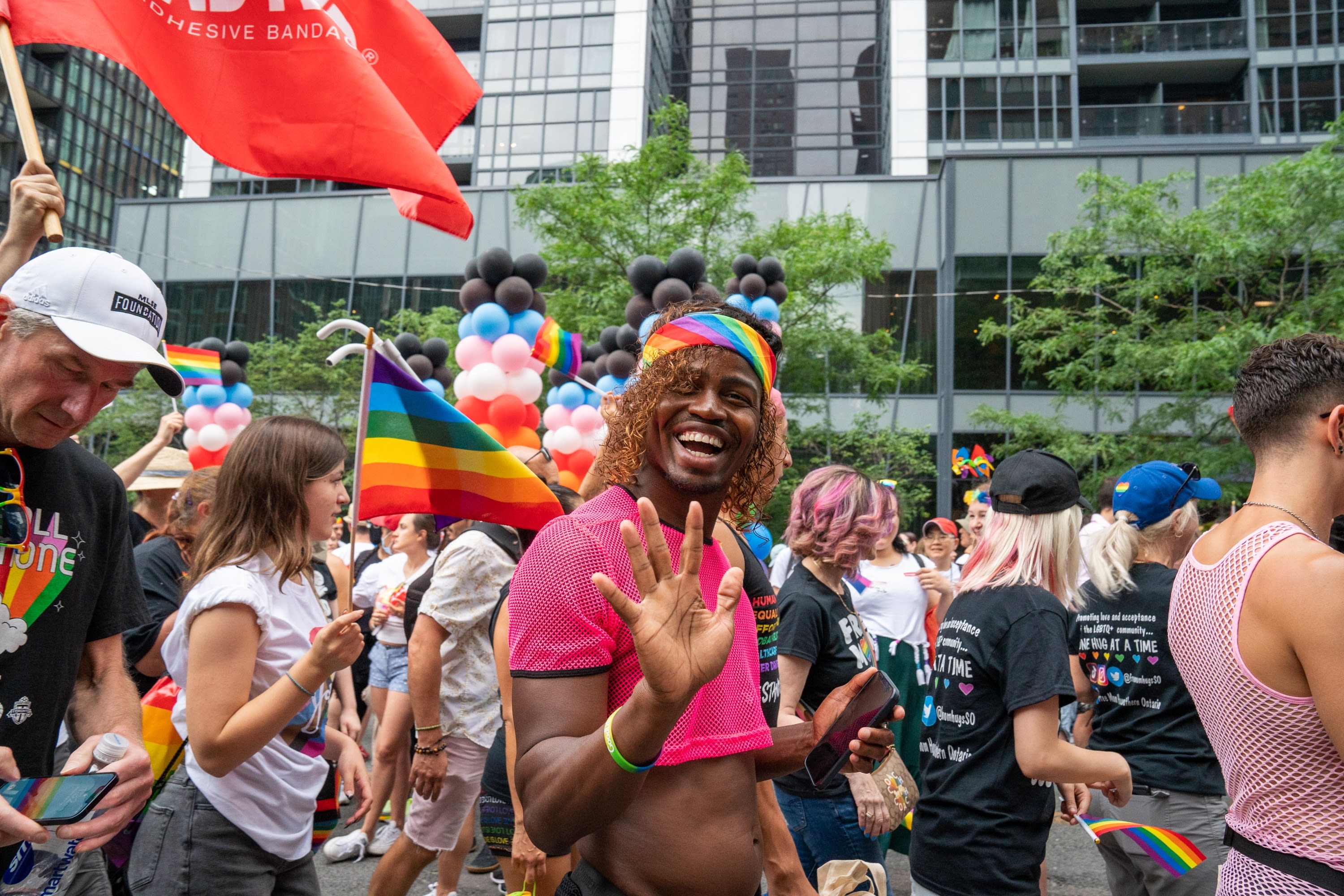 Person at Pride parade surrounded by people, smiling and waving