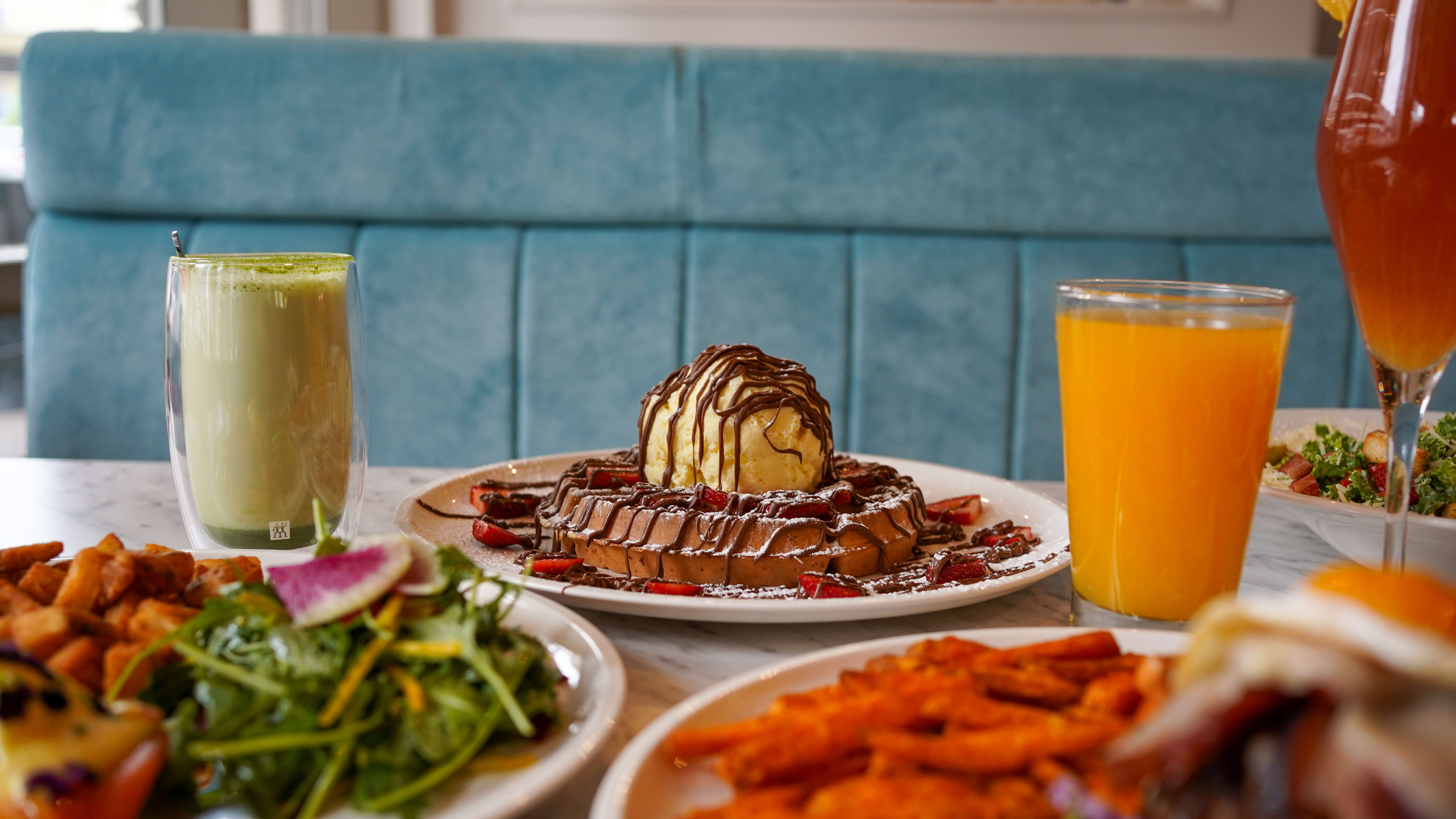 Table of breakfast spread featuring a waffle with ice cream, green smoothie and orange juice.