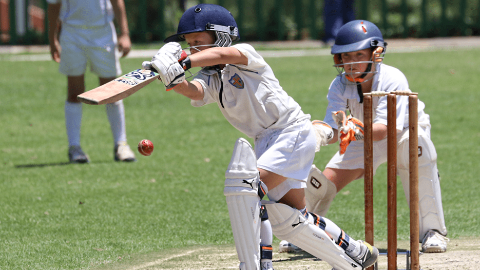 Two young boys play cricket, one mid swing and the other positioned behind as a catcher