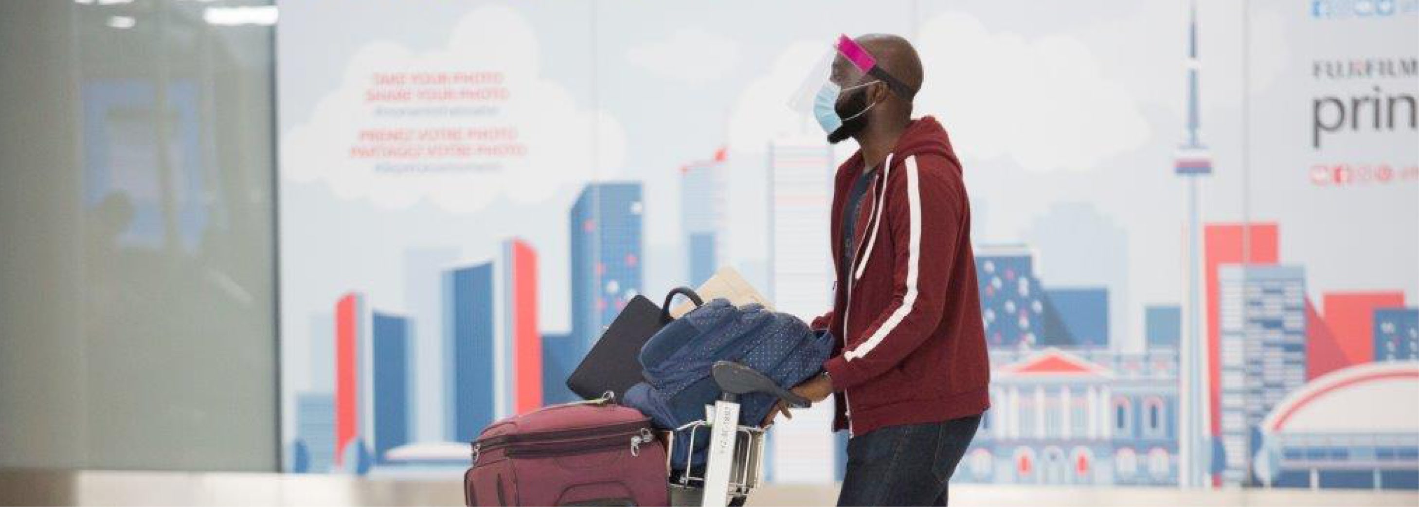 Man pushing luggage while wearing a face covering