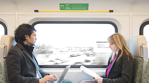 A man, left, sits GOTrain seat looking out the window. Directly across, a women reads a magazine.