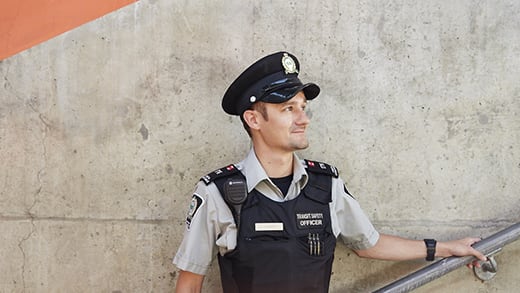 Male Transit Safety Officer standing on stairs holding railing in full uniform.